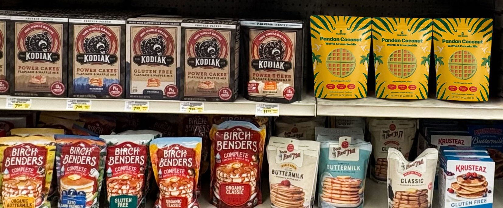 Mockup of the Wasi Brands CPG packaging design displayed on a grocery shelf among competing pancake and waffle mixes, illustrating its visual differentiation within the category.