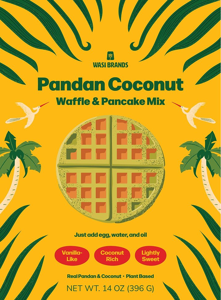 Front of the Wasi Brands Pandan Coconut Waffle & Pancake Mix package with illustrated pandan leaves framing a central waffle, alongside palm trees and Vietnamese Lạc birds on a bright yellow background.