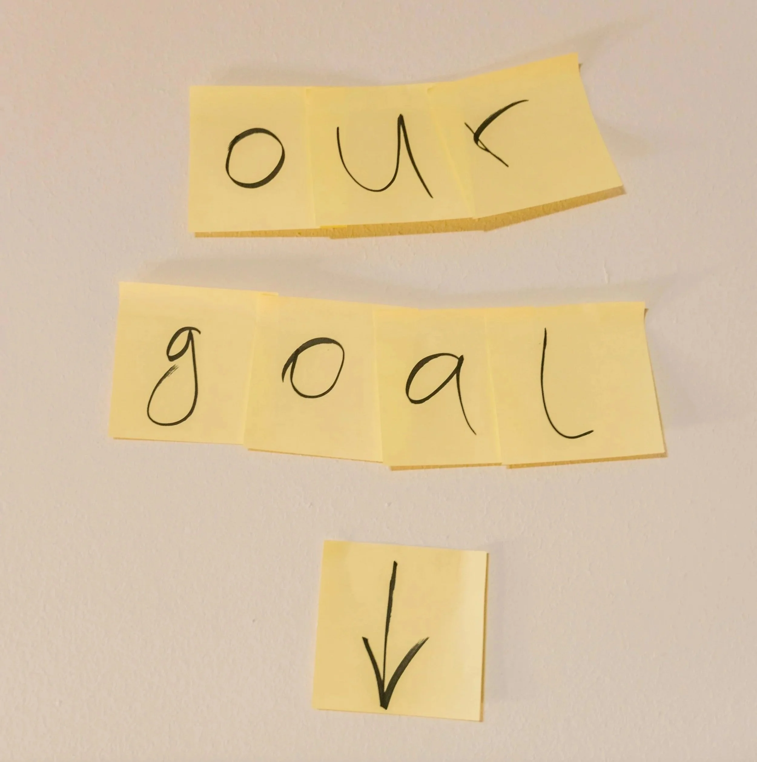 Sticky notes arranged to spell “our goal” with an arrow pointing downward, representing brand strategy workshop.