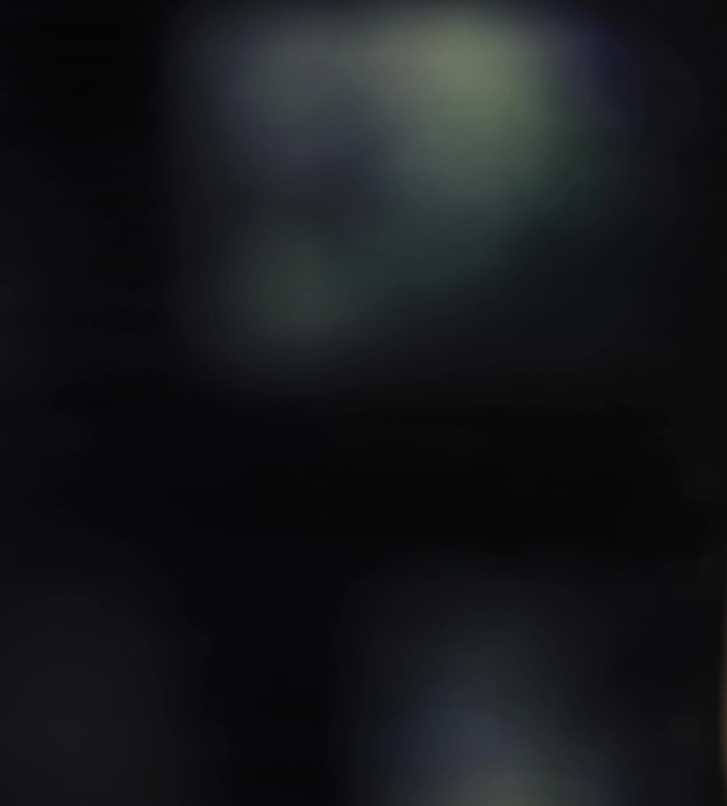 The image is a blurred, dark background with faint, circular, multicolored lights or reflections.