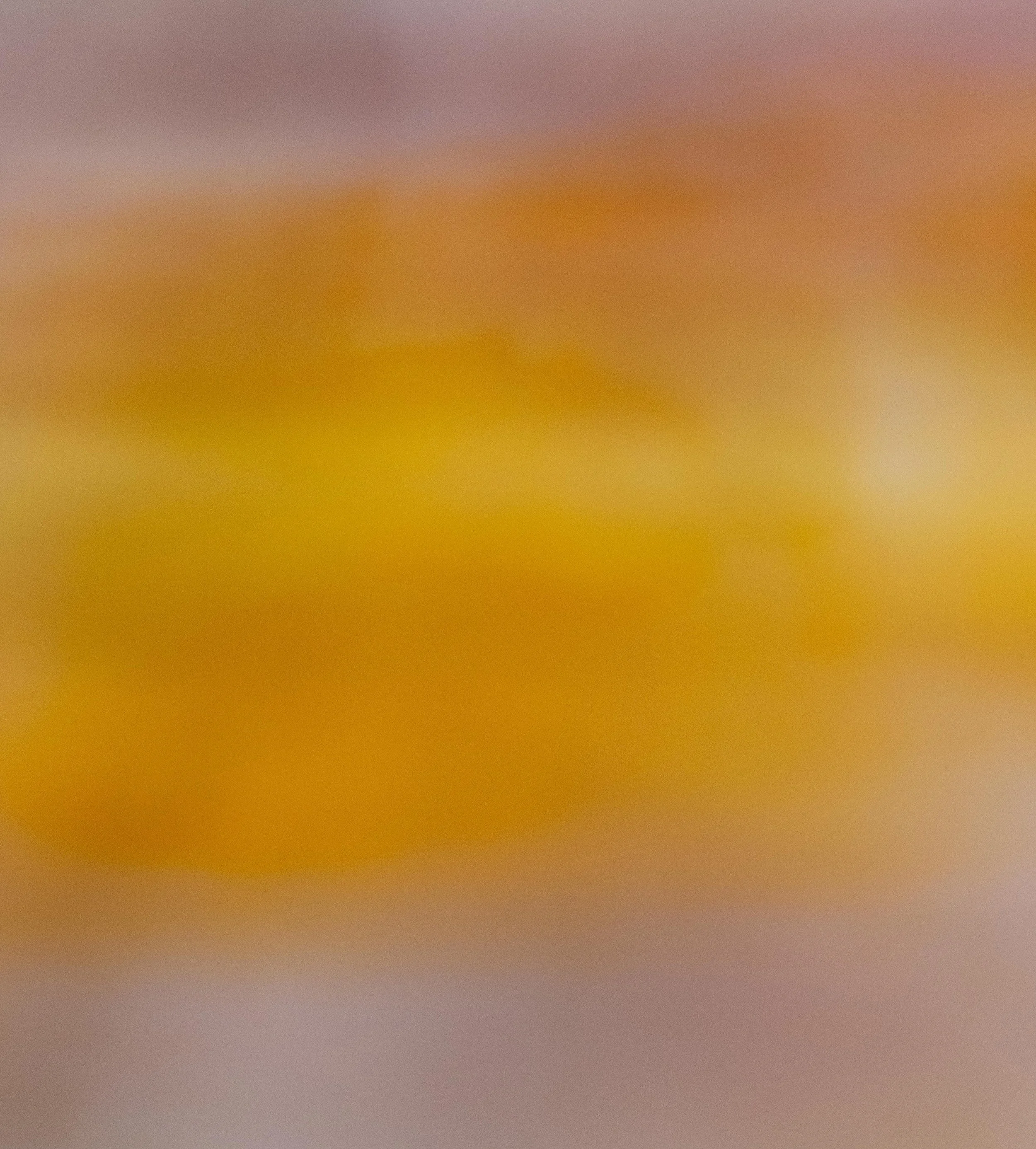 A blurred close-up of a colorful, textured surface with shades of purple, pink, yellow, and orange.