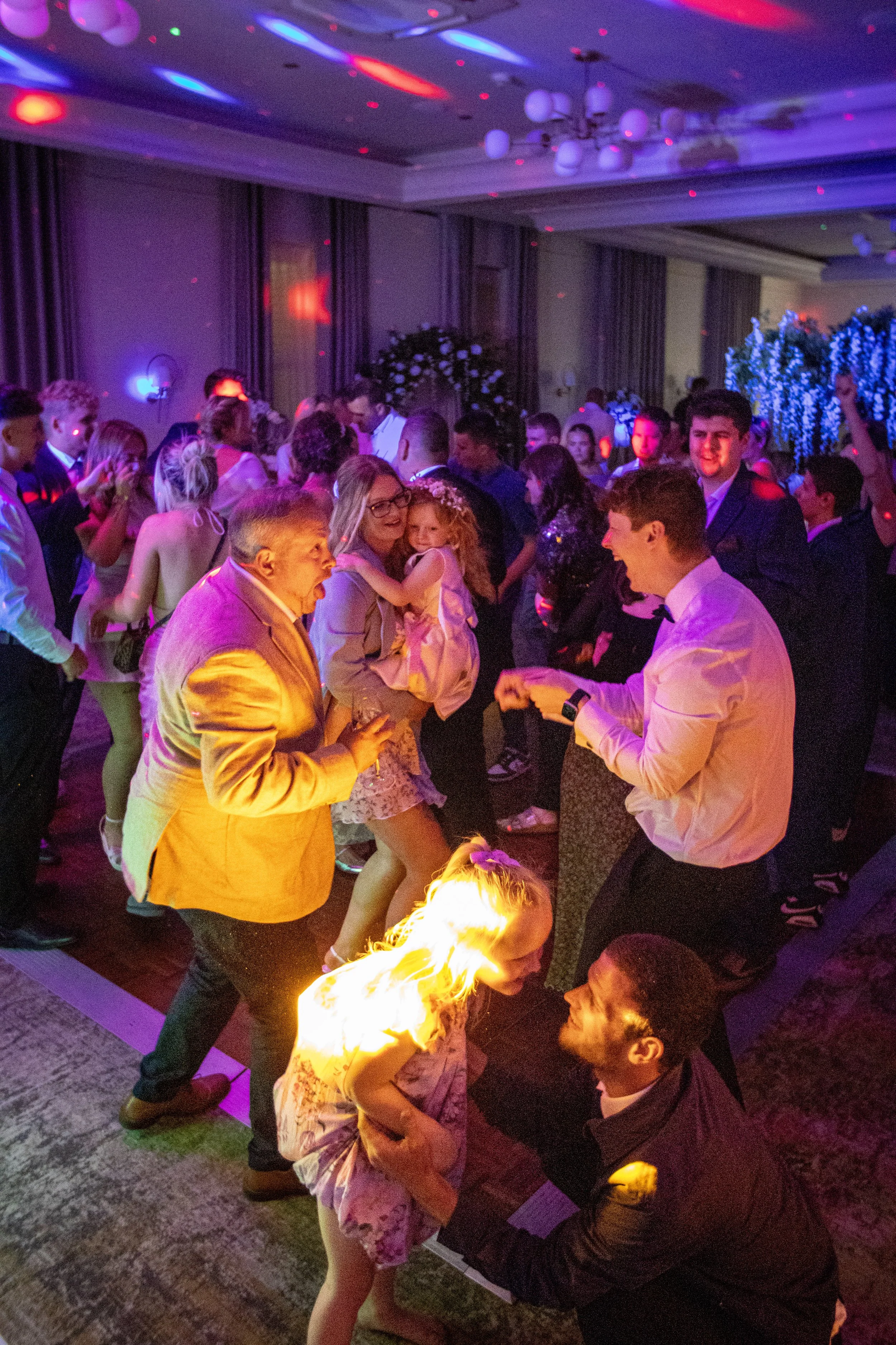 People dancing and enjoying music at a party or celebration in a decorated indoor venue with colorful lights.