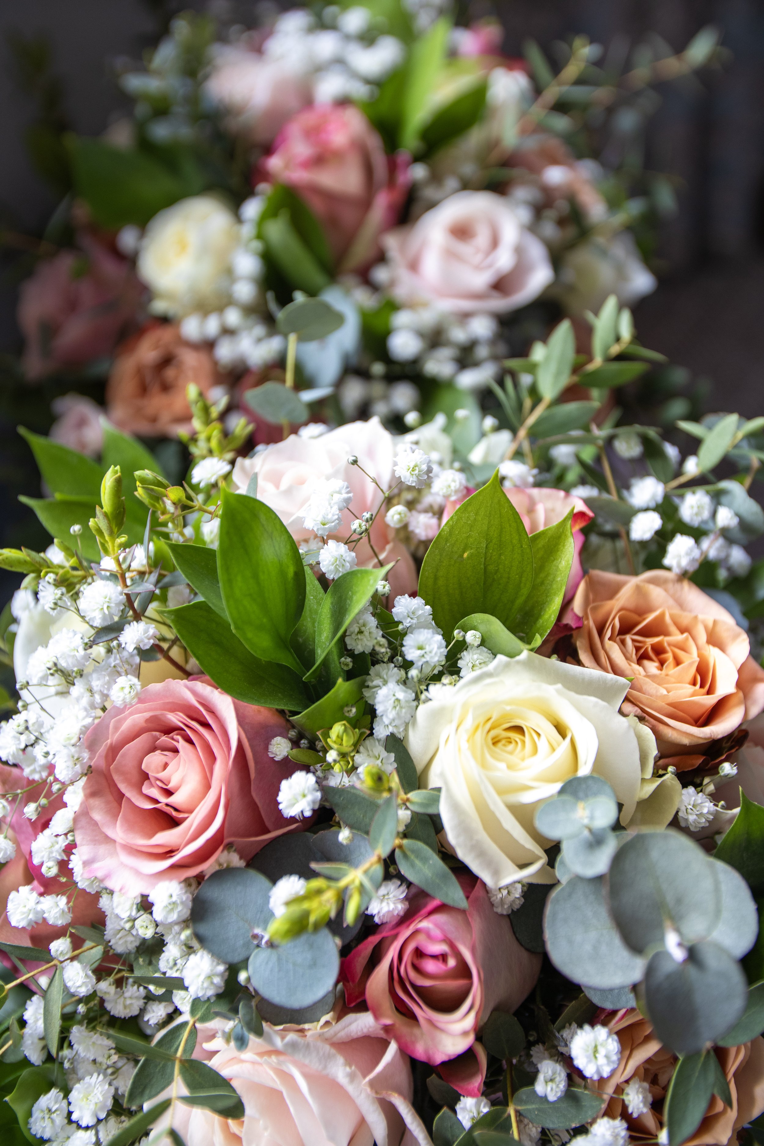 A colorful bouquet of pink, white, and peach roses with white baby's breath and green foliage.
