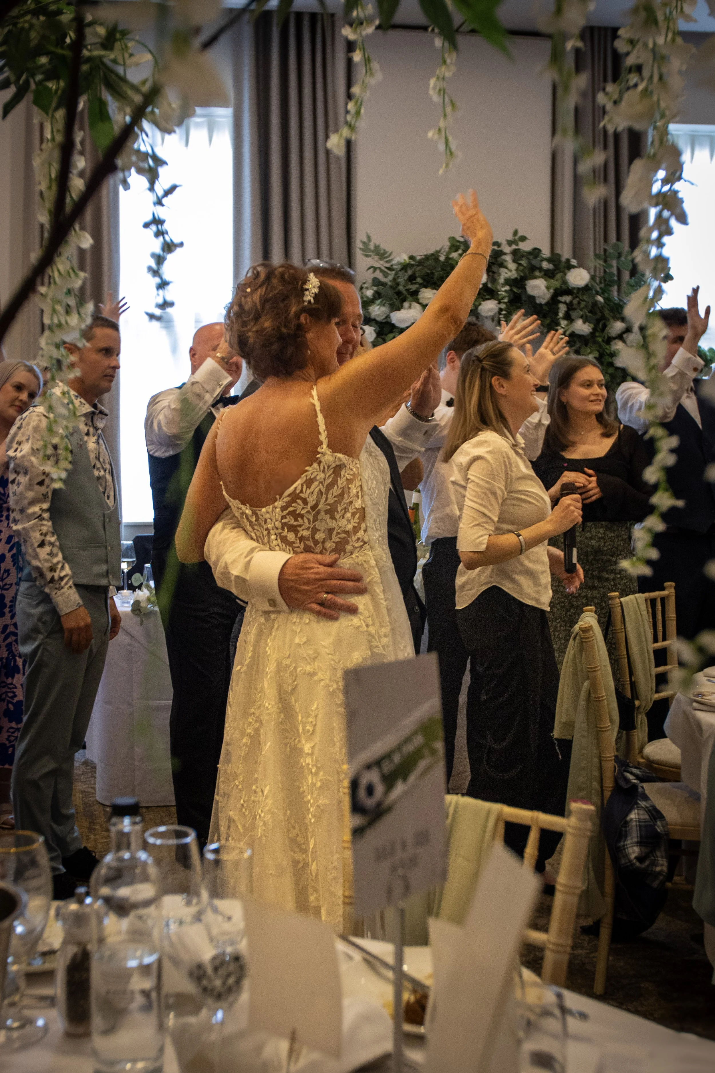 People at a wedding reception, dancing and enjoying themselves in a decorated indoor venue with floral arrangements.
