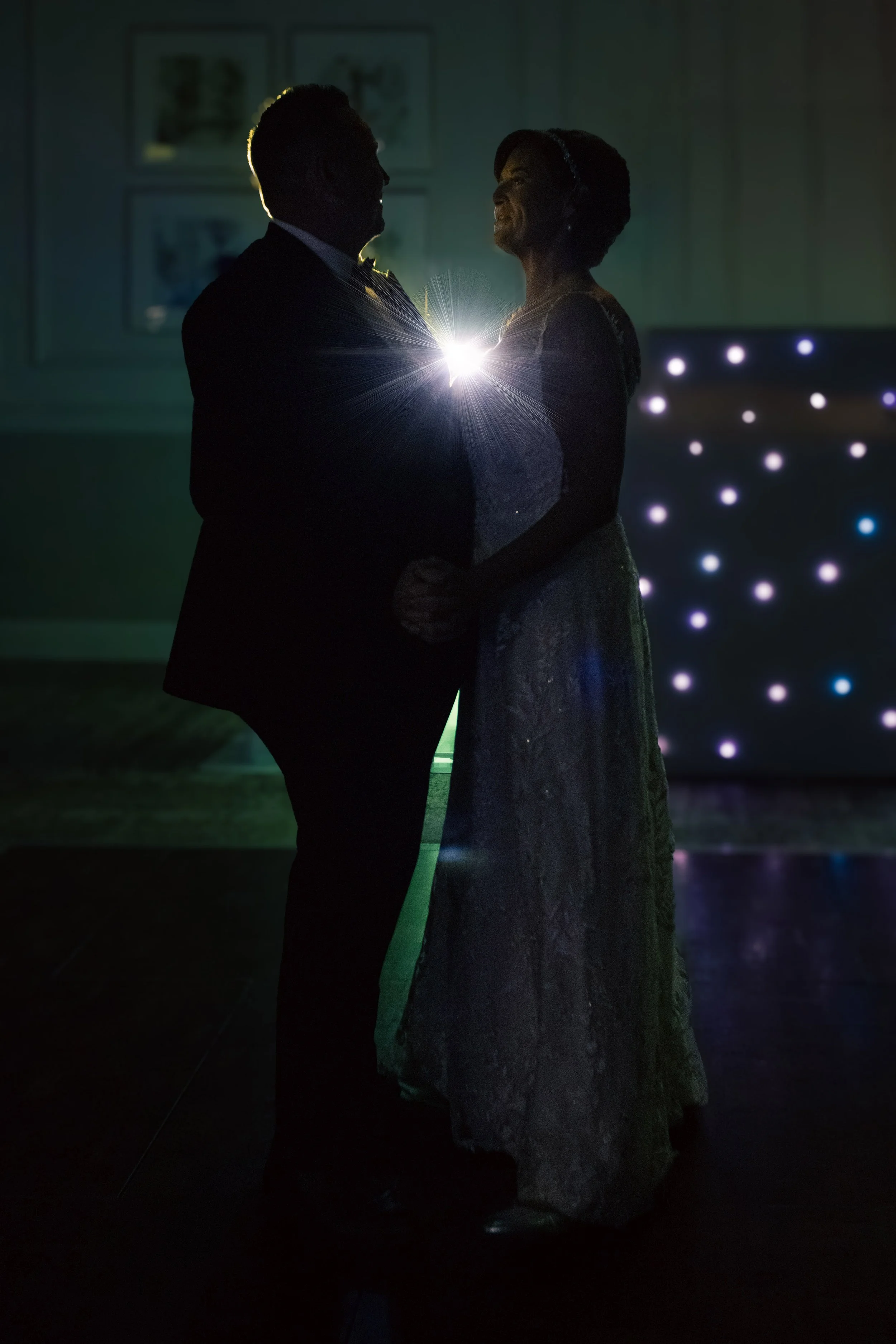 A silhouetted couple dancing closely in a dimly lit room with a spark of light between them, creating a romantic atmosphere.
