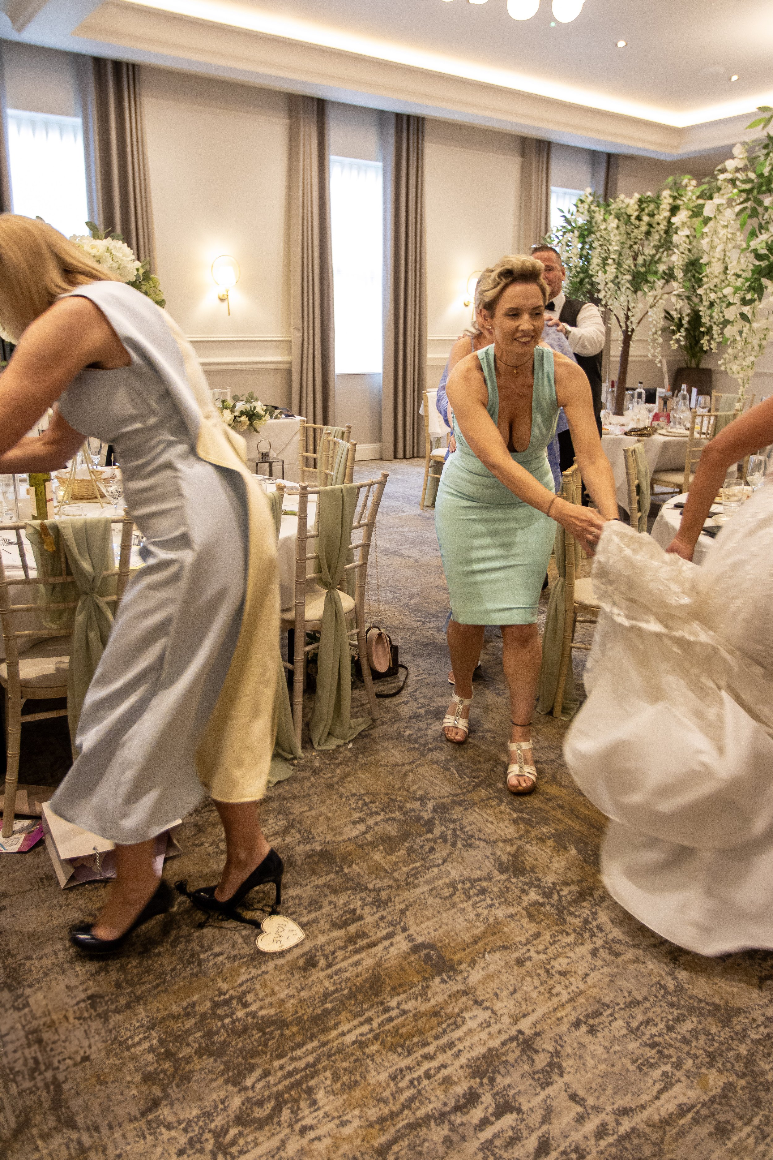 A woman in a turquoise dress walking on a patterned carpet at a wedding reception, surrounded by tables with chairs and floral decorations.