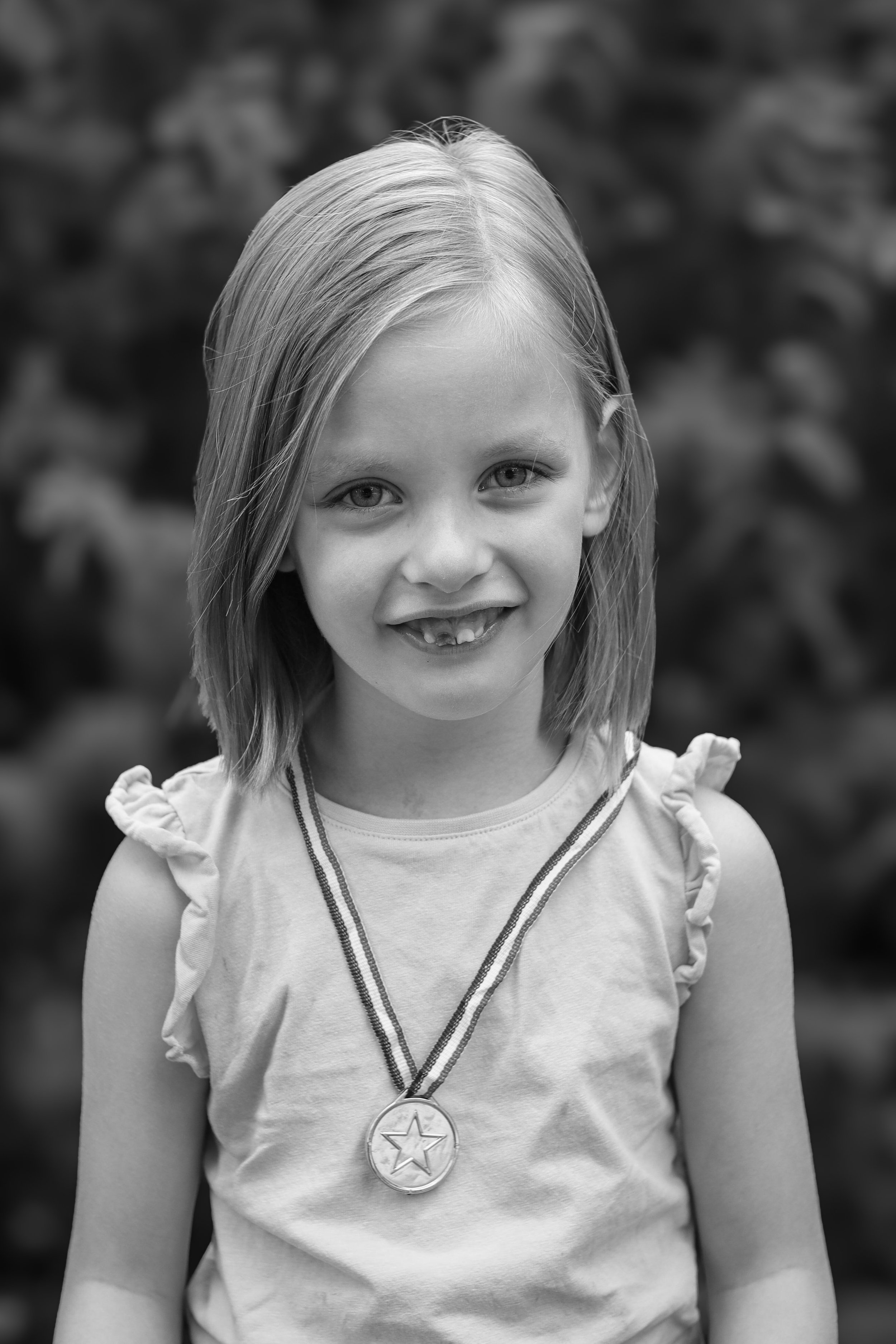 A young girl with shoulder-length hair wearing a sleeveless top with ruffled shoulders and a medal around her neck, smiling at the camera.