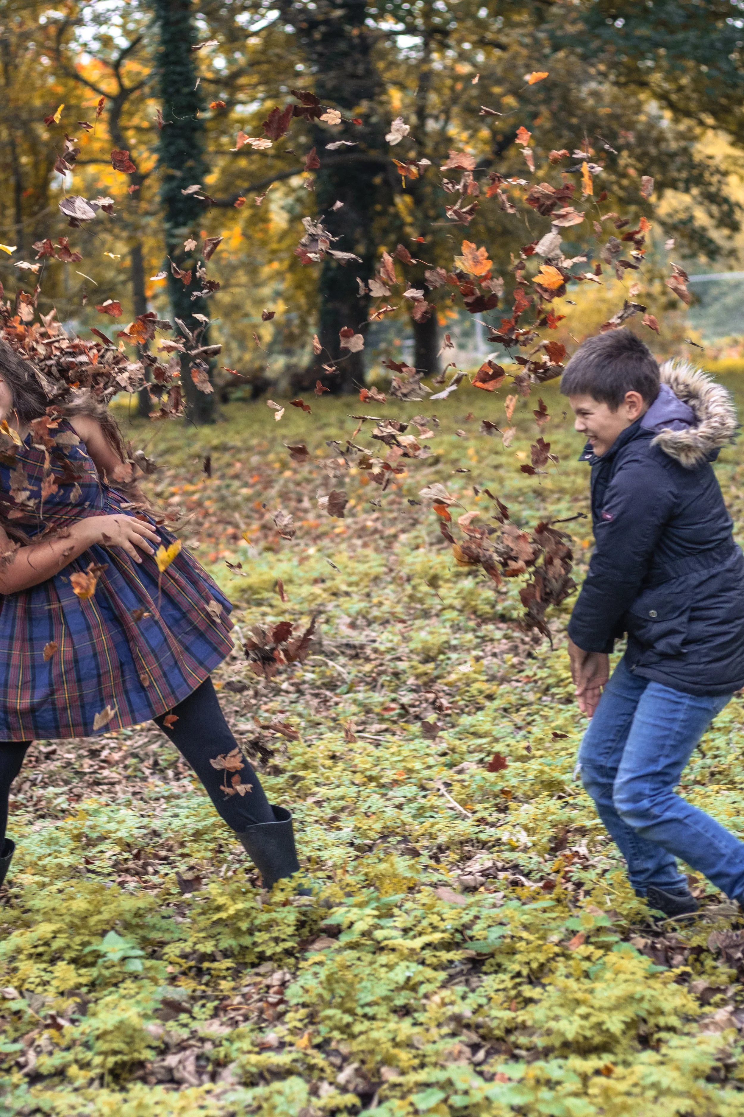 Children playing in a park on a fall day, throwing leaves into the air and smiling.