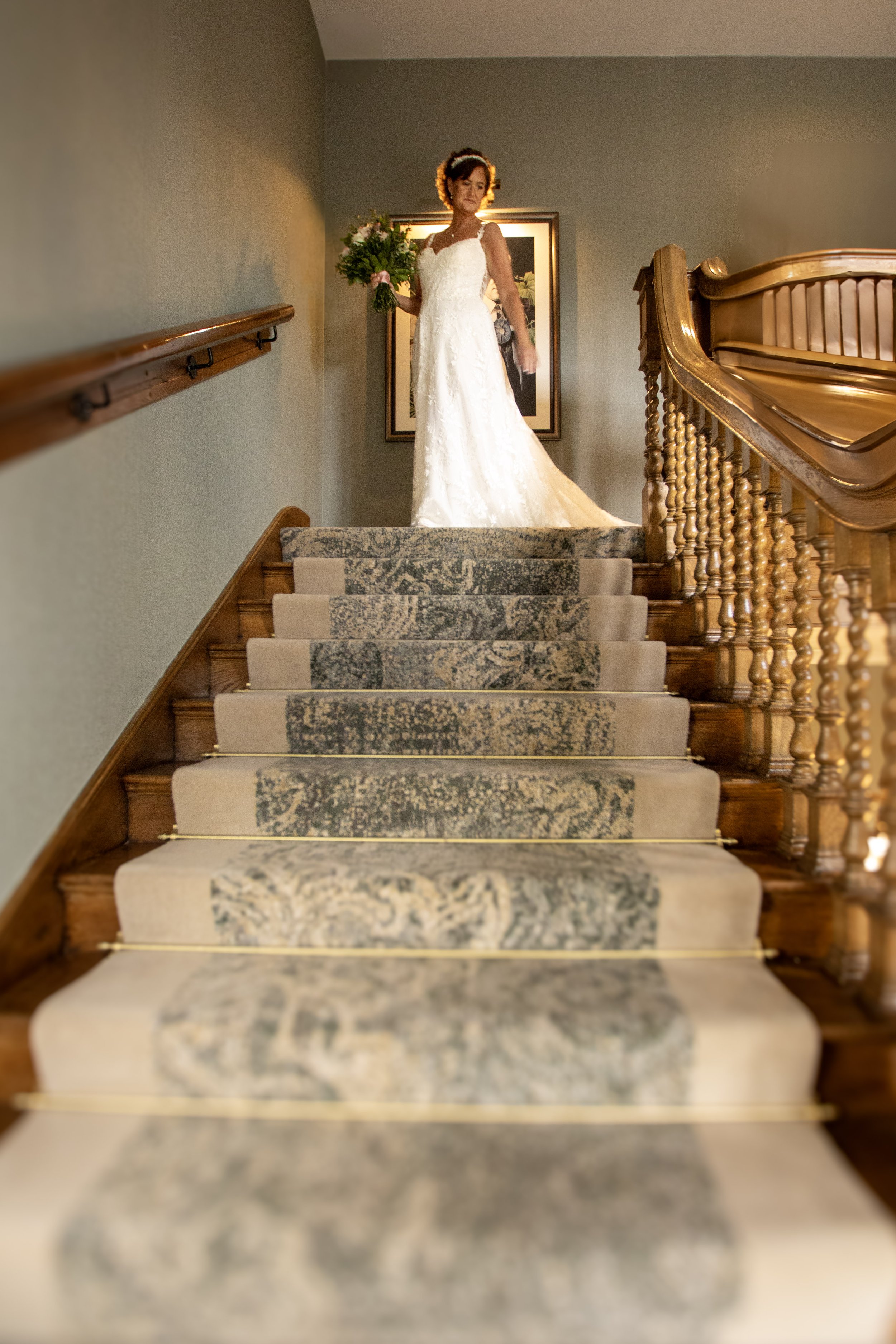 A woman in a white wedding dress standing at the top of a staircase, holding a bouquet of flowers.