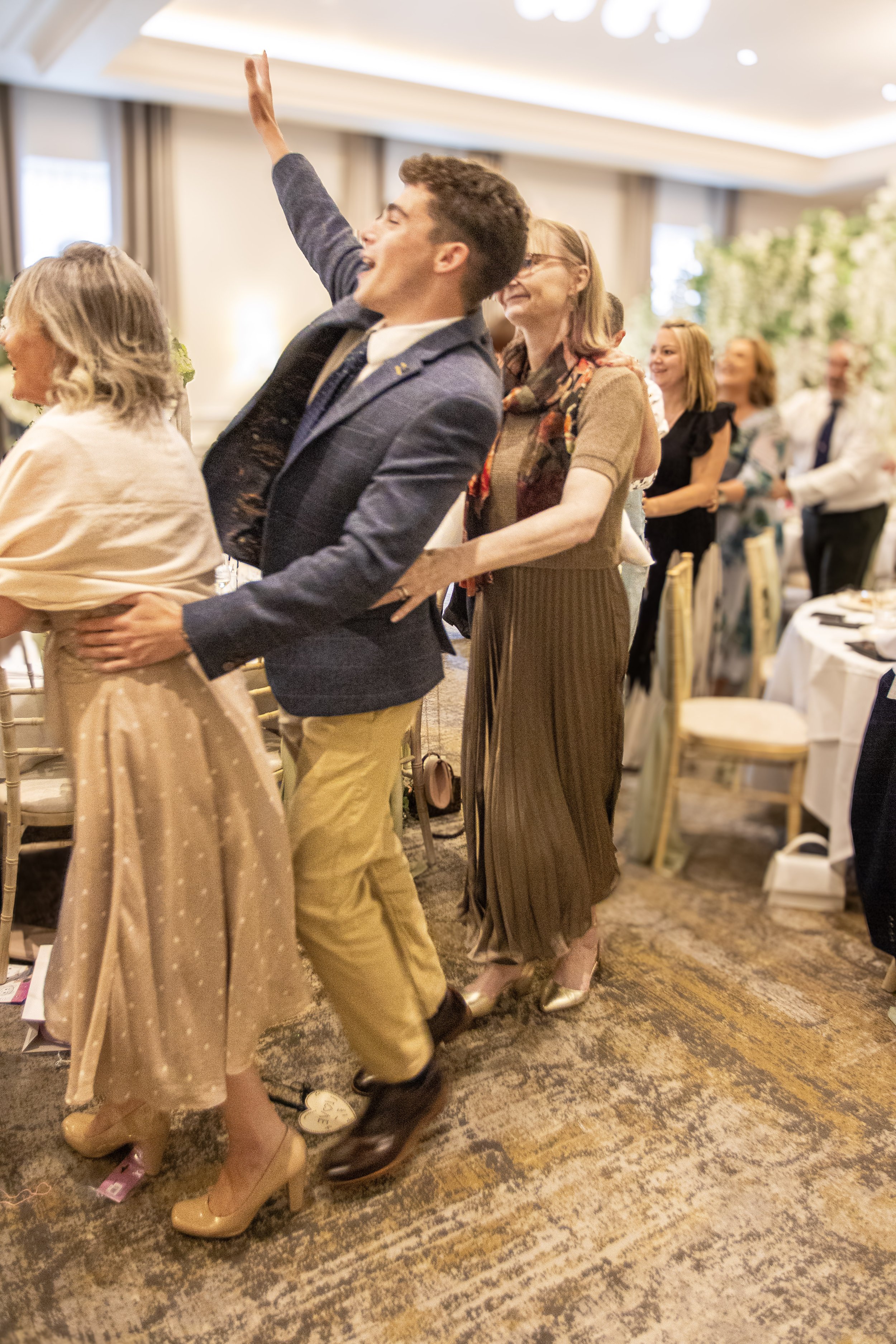 People dancing in a conga line at a celebration event in a banquet hall.