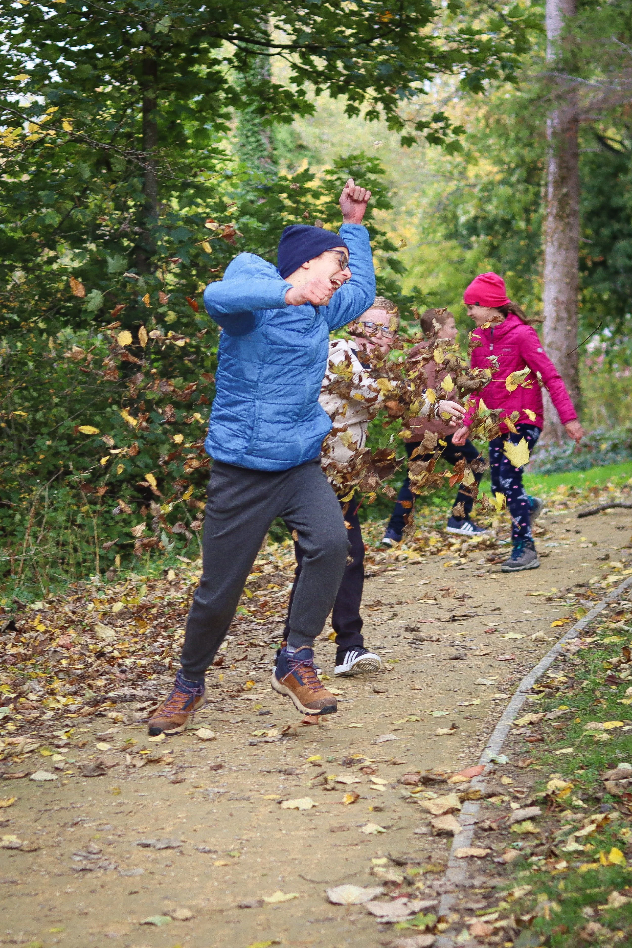 Children playing and throwing leaves on a forest path during fall.