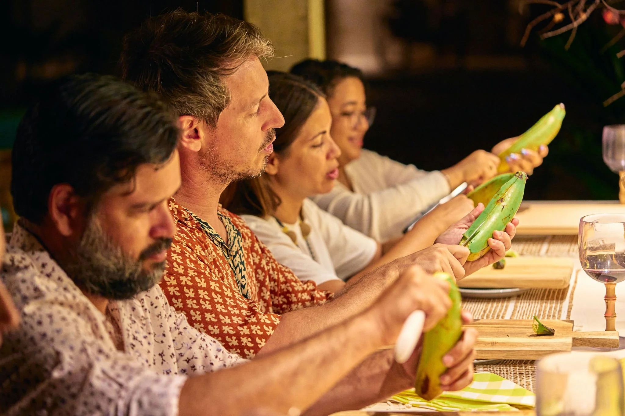 Varias personas sentadas en la mesa pelando plátanos en una comida compartida.