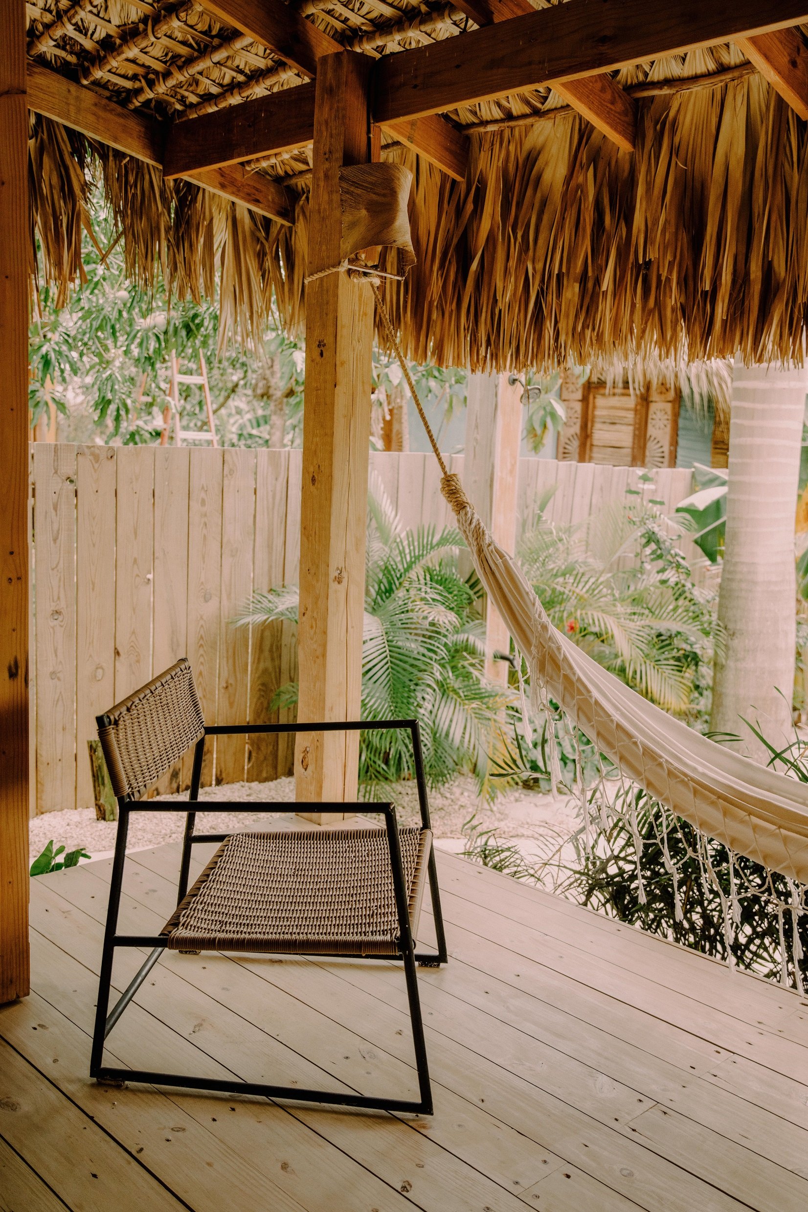 Tobogán de cuerda colgando de una estructura de madera en una terraza con sillas, en un ambiente tropical con plantas verdes y palmeras.