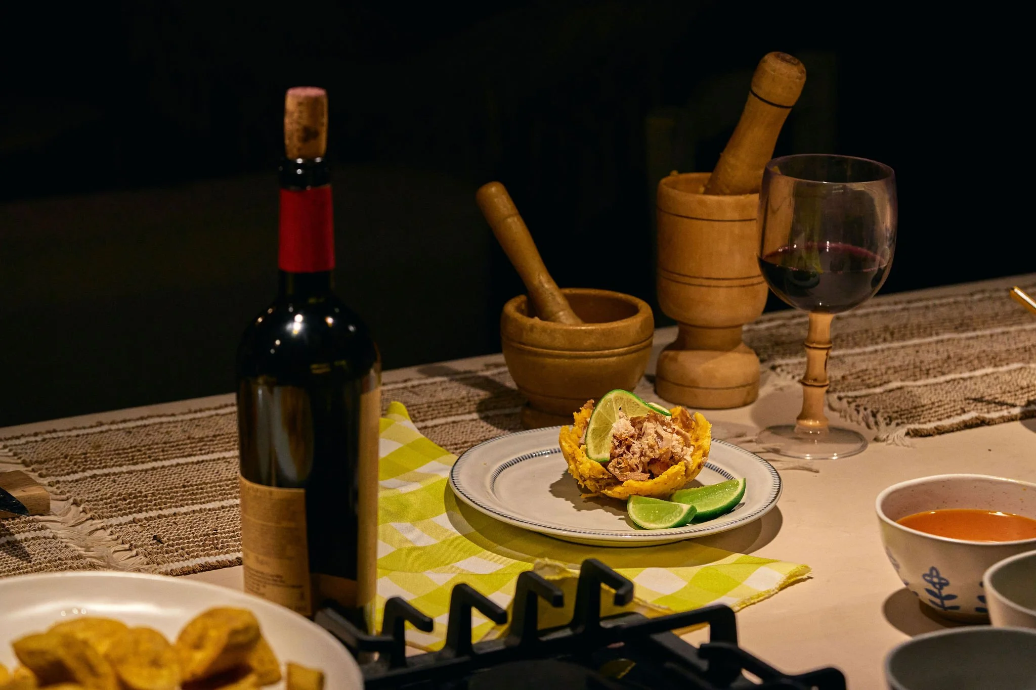 Plato con comida, copas de vino tinto, morteros de moler, y una botella de vino en una mesa de cena