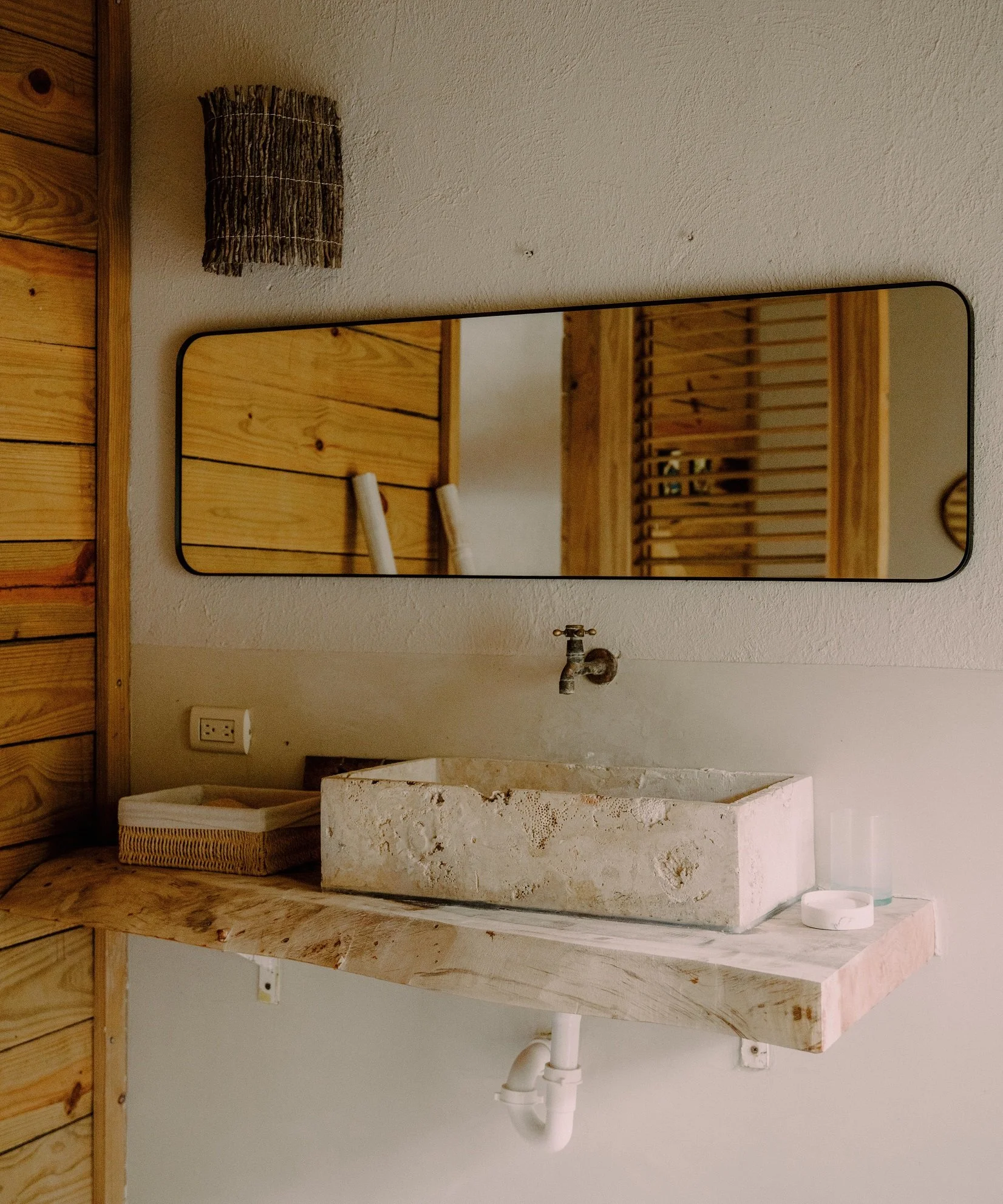 Lavabo de piedra en un baño con espejo rectangular y pared de madera.