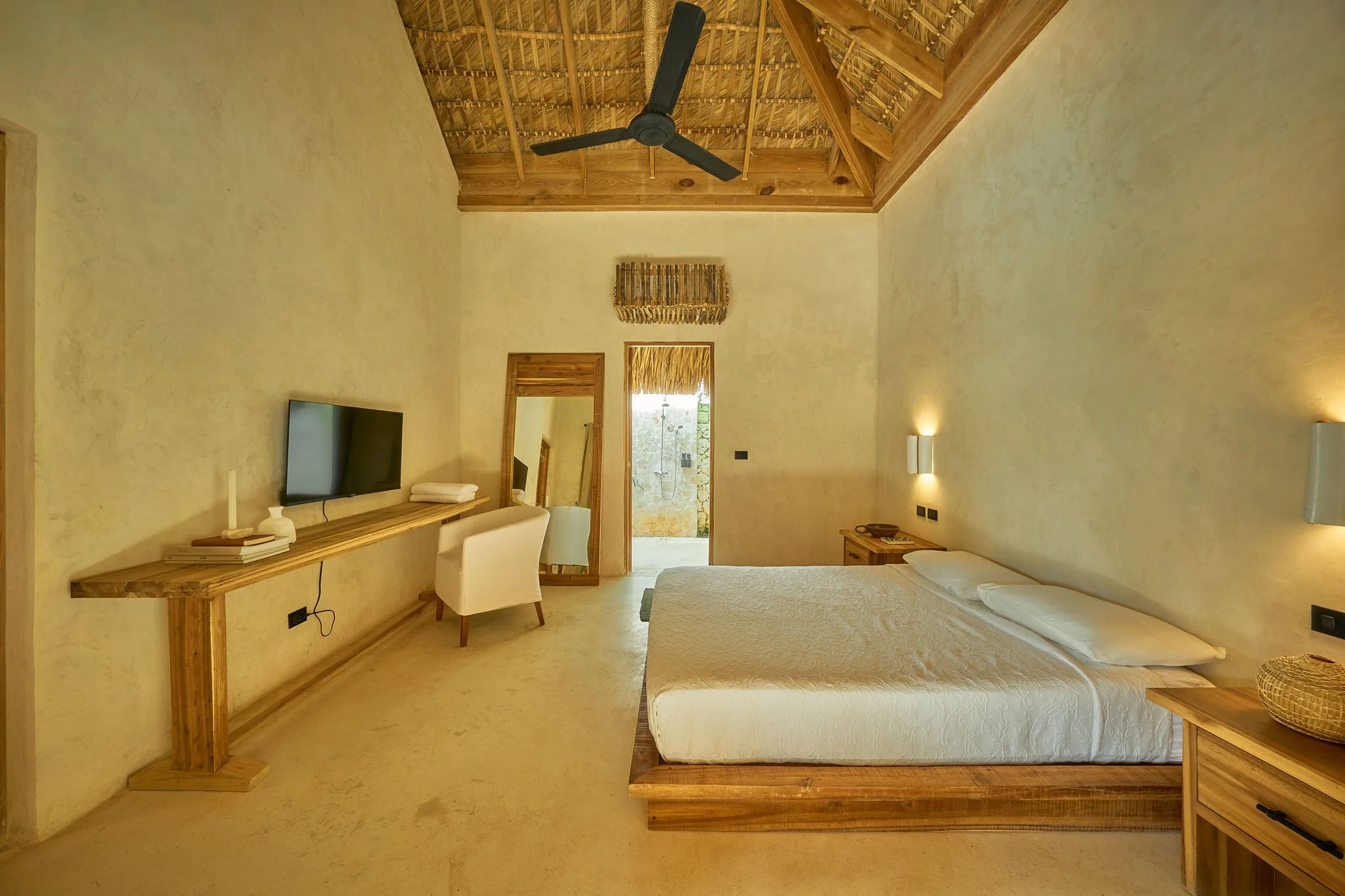 Habitación de estilo rústico con cama doble, paredes beige, mobiliario de madera, televisor y ventilador en el techo.