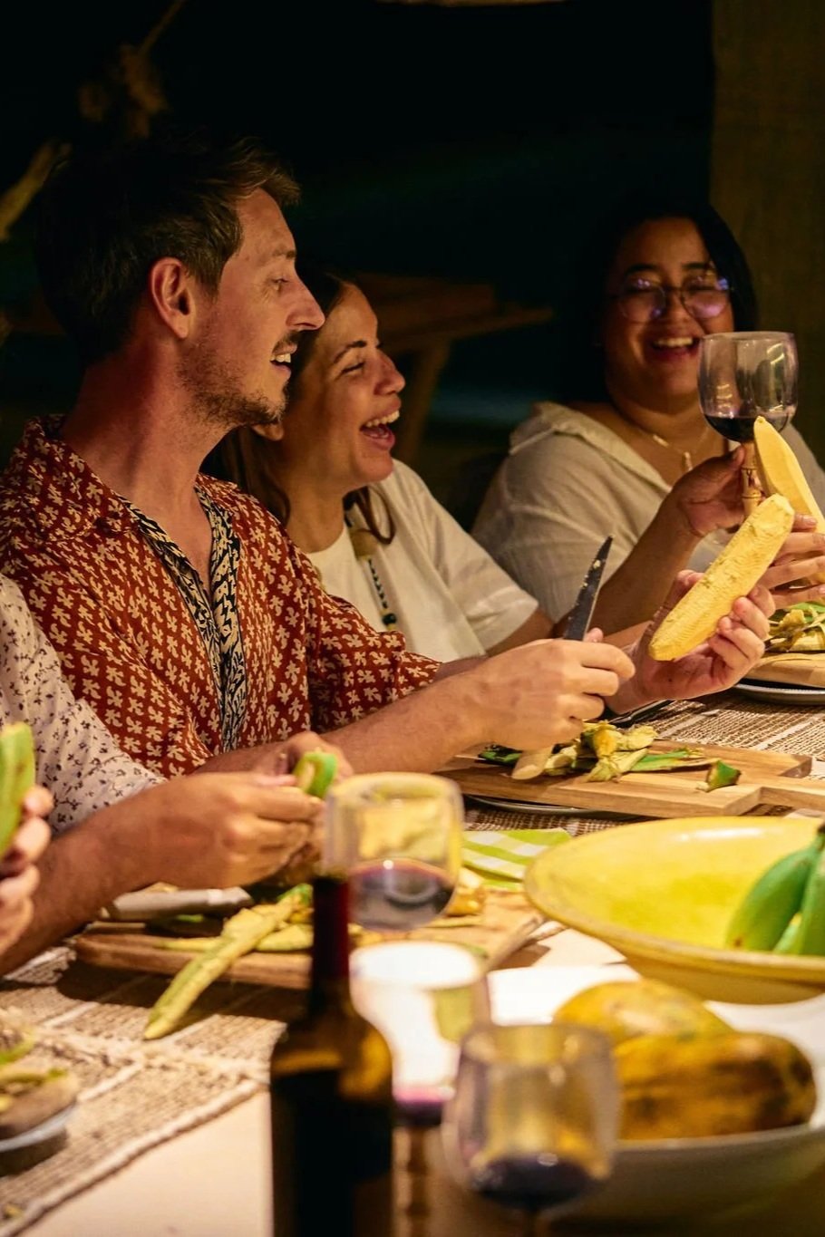 Personas disfrutando de una cena en una mesa con comida y vino, riendo y conversando.
