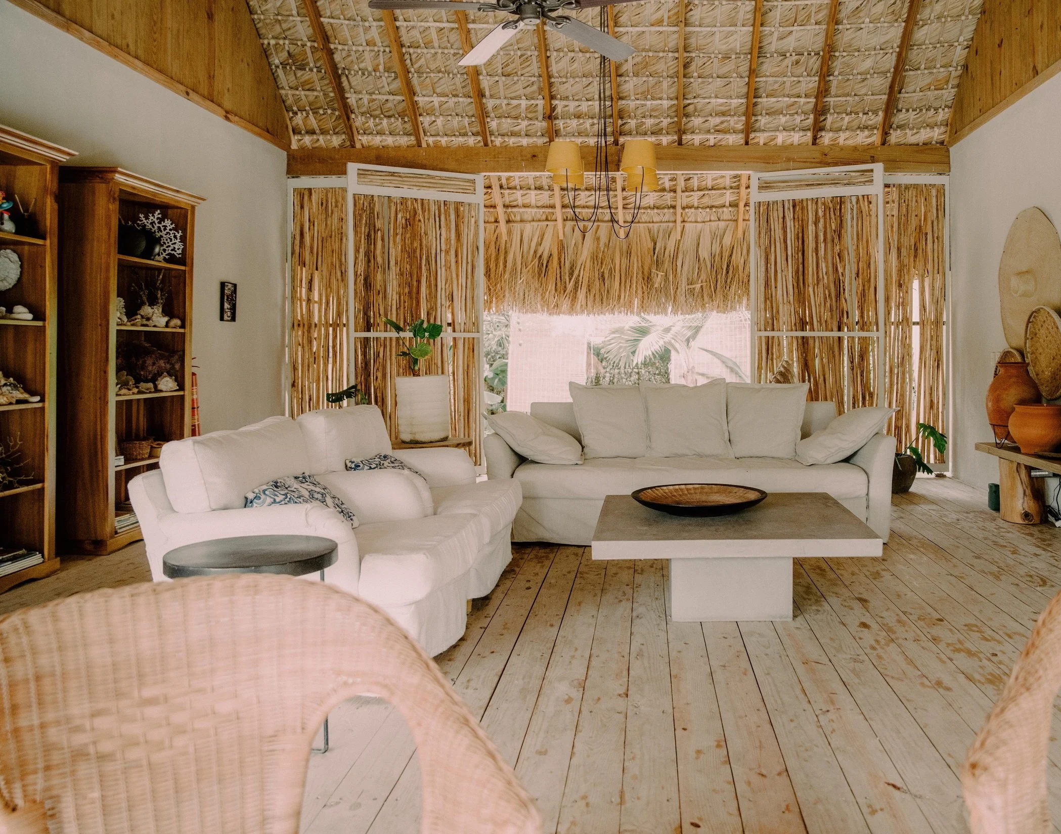 Sala de estar con muebles blancos, estanterías de madera, paredes de madera y decoraciones de estilo natural y rústico, con plantas y accesorios de cerámica.