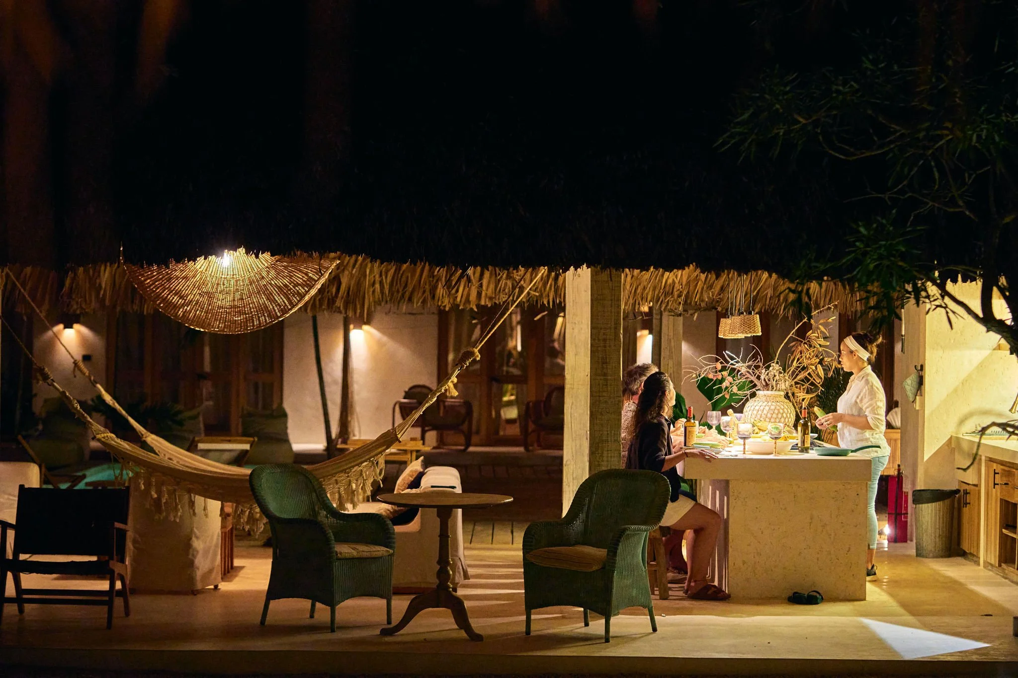 Personas cenando en un restaurante al aire libre, con ambiente cálido y decoraciones tropicales de noche.