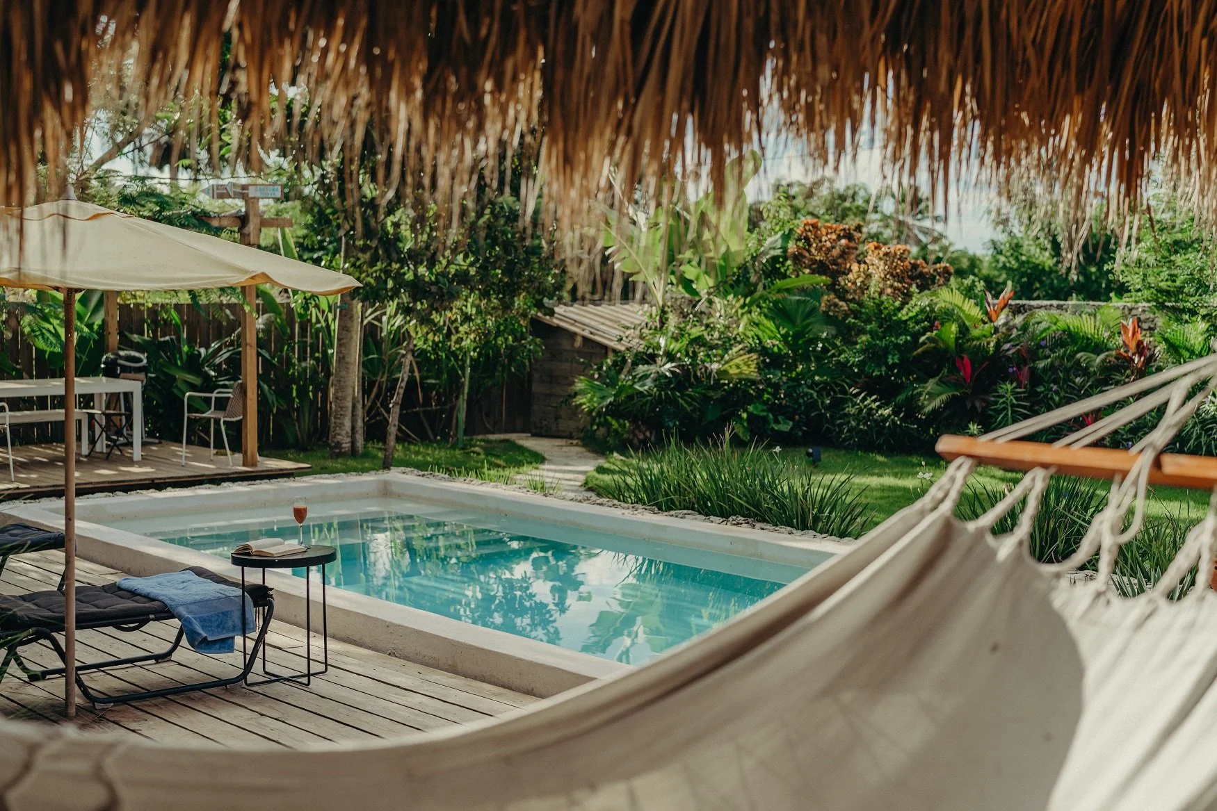 Zona de piscina rodeada de vegetación, con hamaca, sombrilla y sillones en un ambiente al aire libre