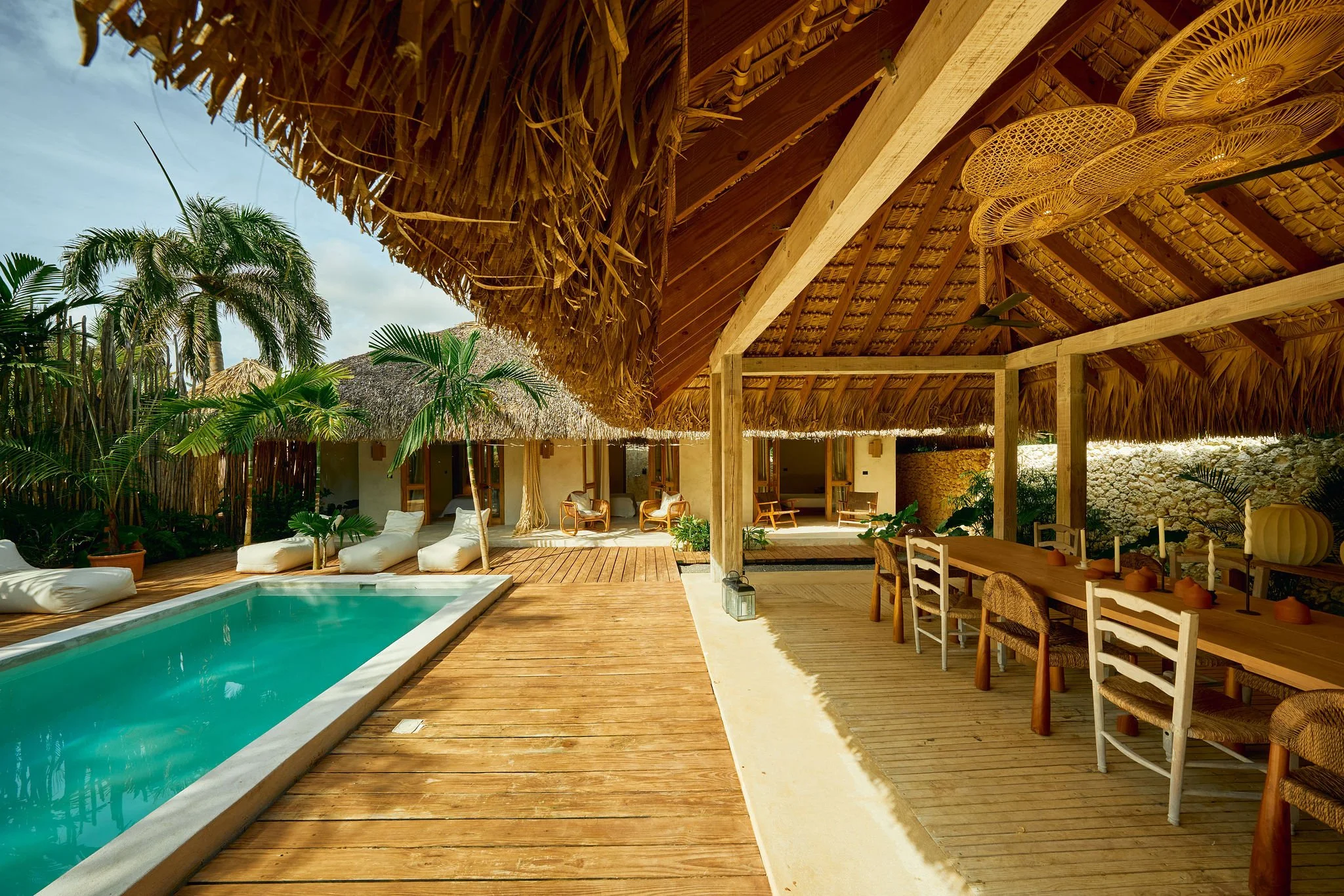 Área de descanso con piscina, sillones, y una estructura de techo de paja en un ambiente tropical