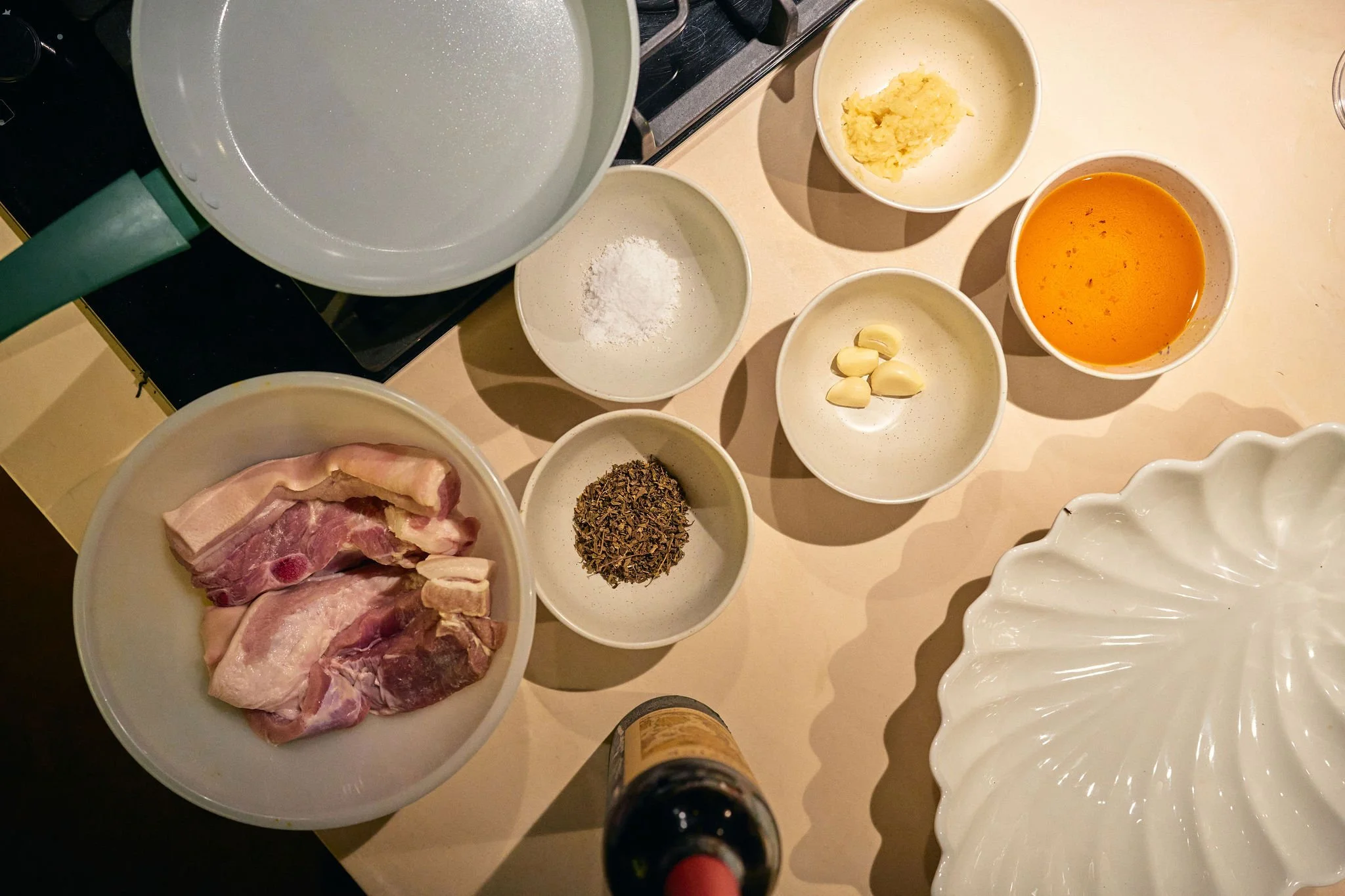 Ingredientes para cocinar, incluyendo carne de cerdo, ajo, hierbas secas, polvo, sal, caldo de pollo, jengibre rallado, pasta, semillas de pimienta y un líquido naranja en un tazón.