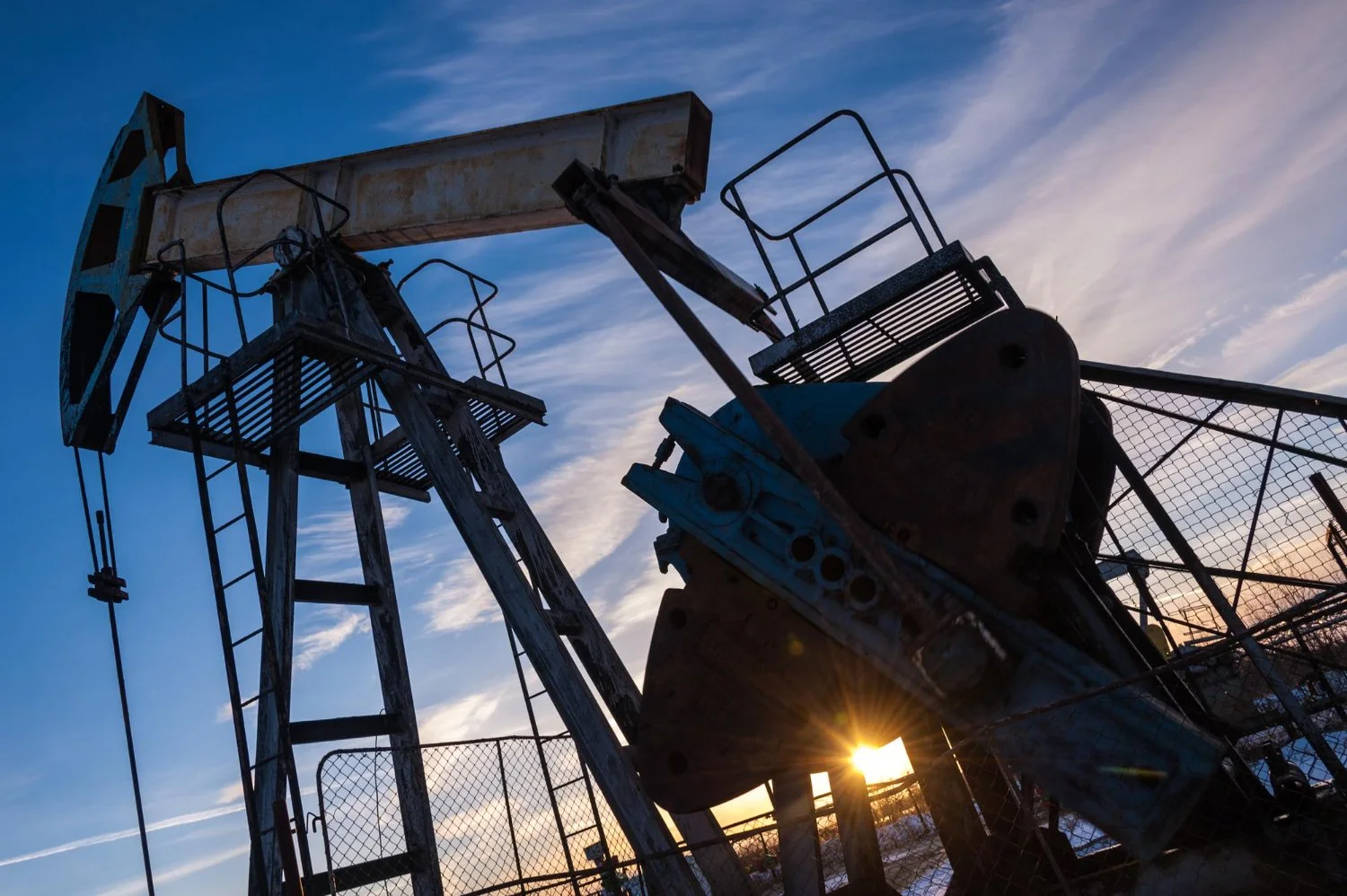 An oil pumpjack silhouette against a sunset sky with clouds.