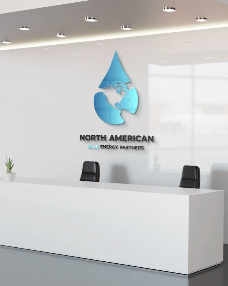 Modern office reception area with a white desk, two black chairs, a small potted plant, and a logo on the wall showing a water droplet with a map of North America inside and the text 'North American Blue Energy Partners'.