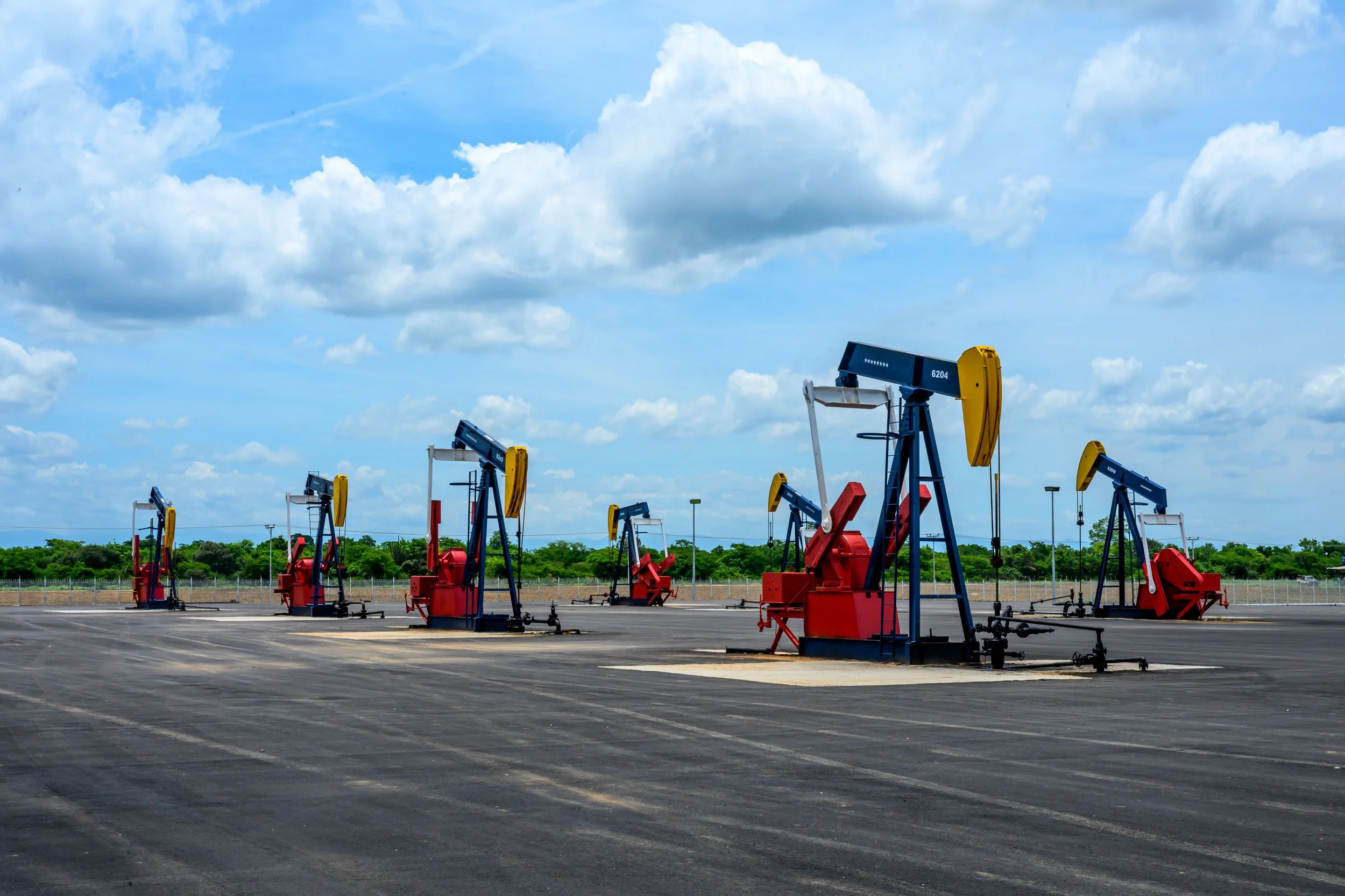 Multiple oil pumpjacks in a row at an oil field under a partly cloudy sky.