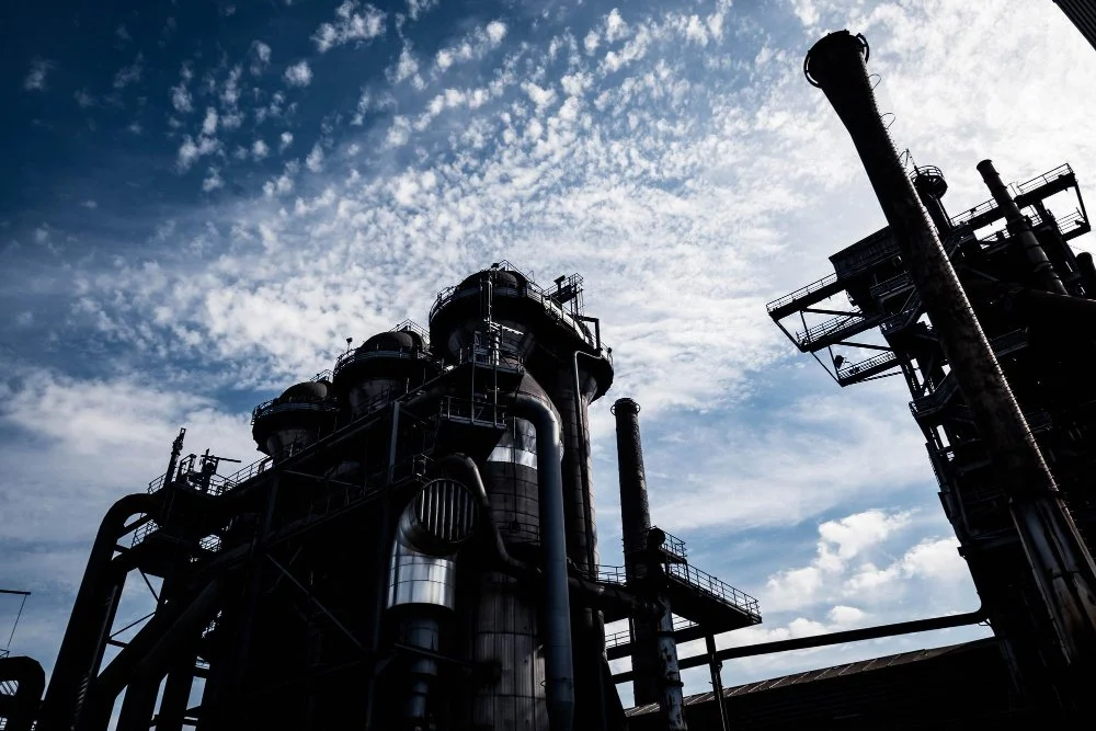 Industrial factory with tall smokestacks and pipes against a partly cloudy sky.