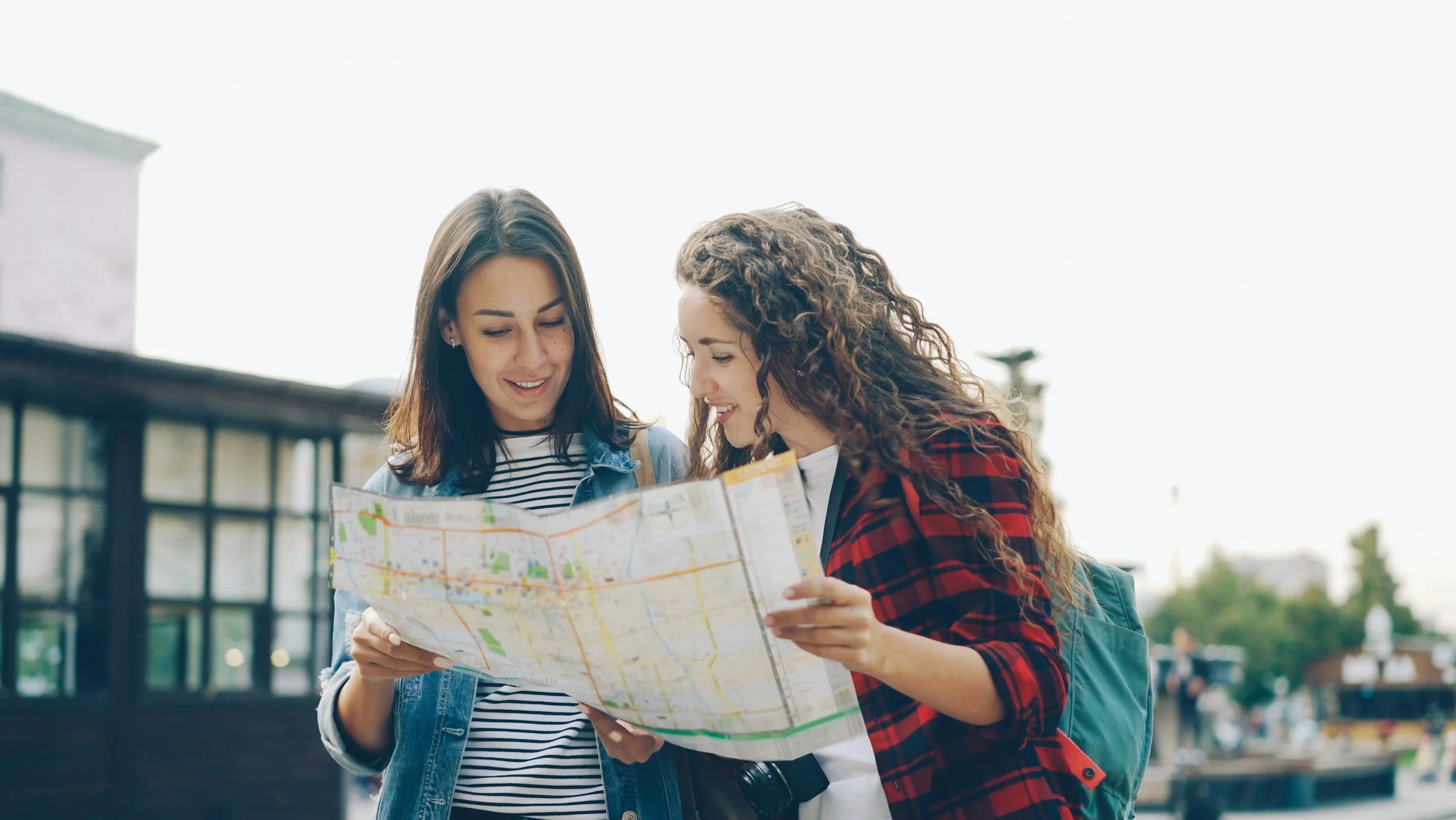 Two young women looking at a city map outdoors, smiling and enjoying their sightseeing.