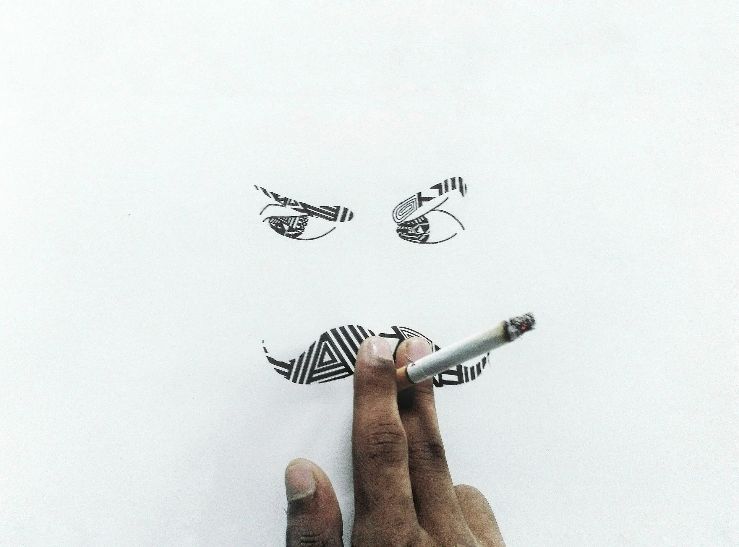A person's hand holding a lit cigarette, drawing a smiley face on a white surface, with eyes and a mouth outlined in black.