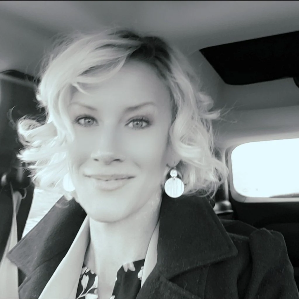 A woman with curly blonde hair and earrings taking a selfie inside a vehicle.