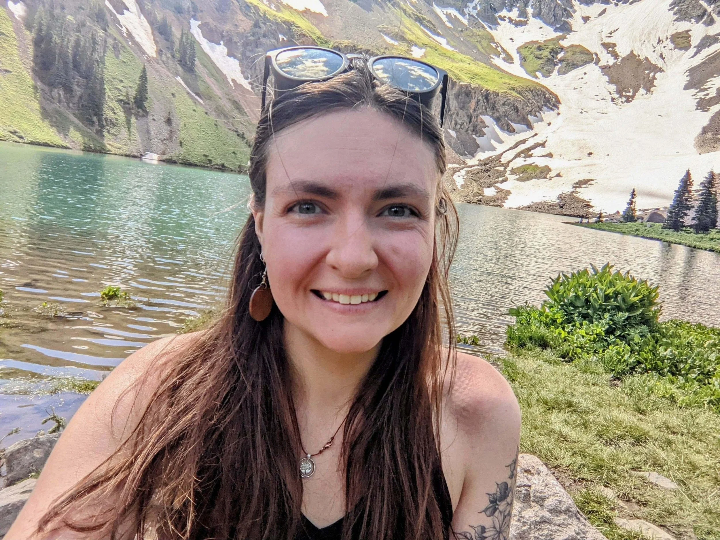 A young woman with long, medium brown hair, wearing a light-colored top and a small necklace, against a black background.