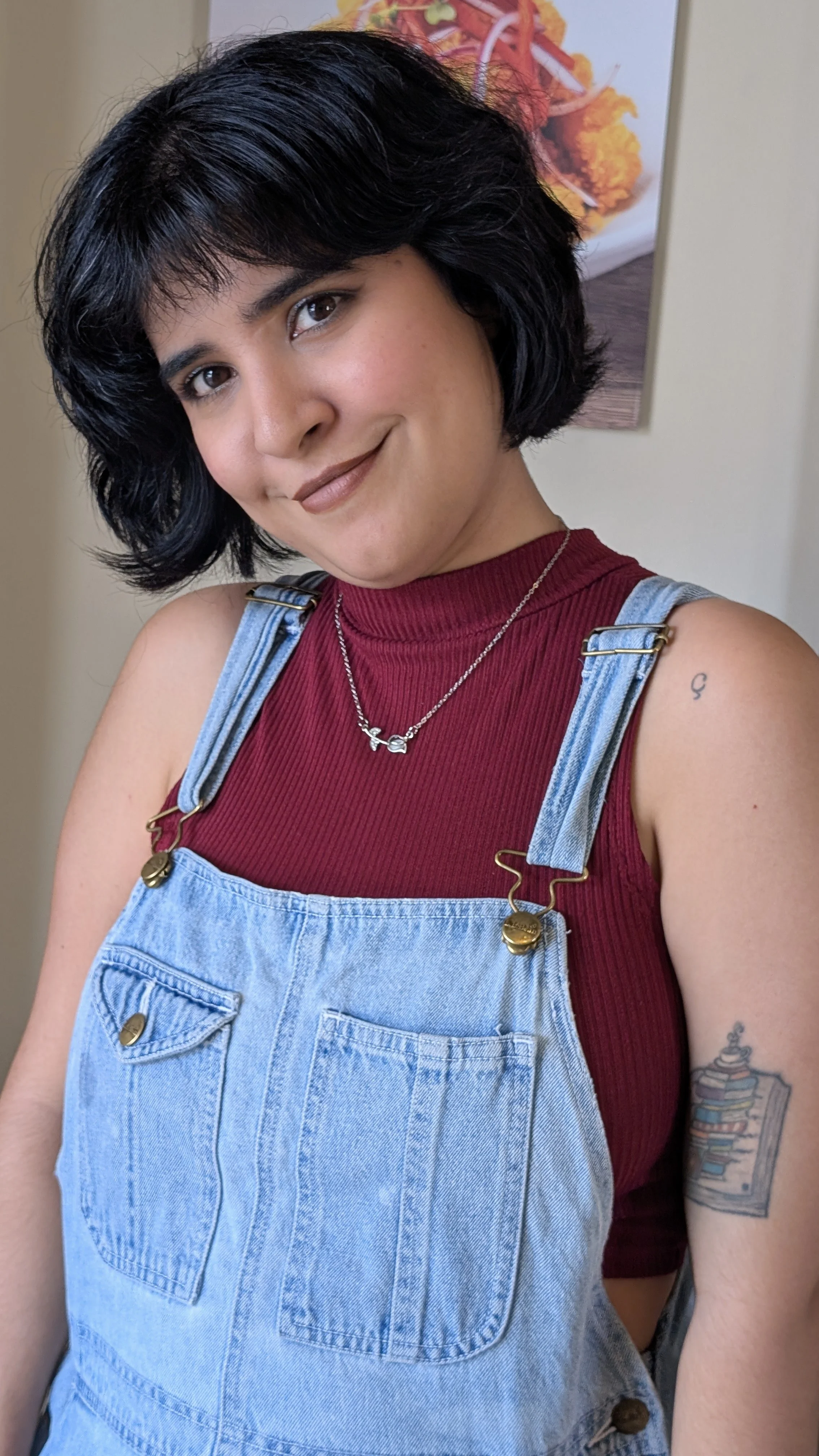 Young woman with short dark hair and glasses smiling and making a peace sign with her right hand in a decorated room