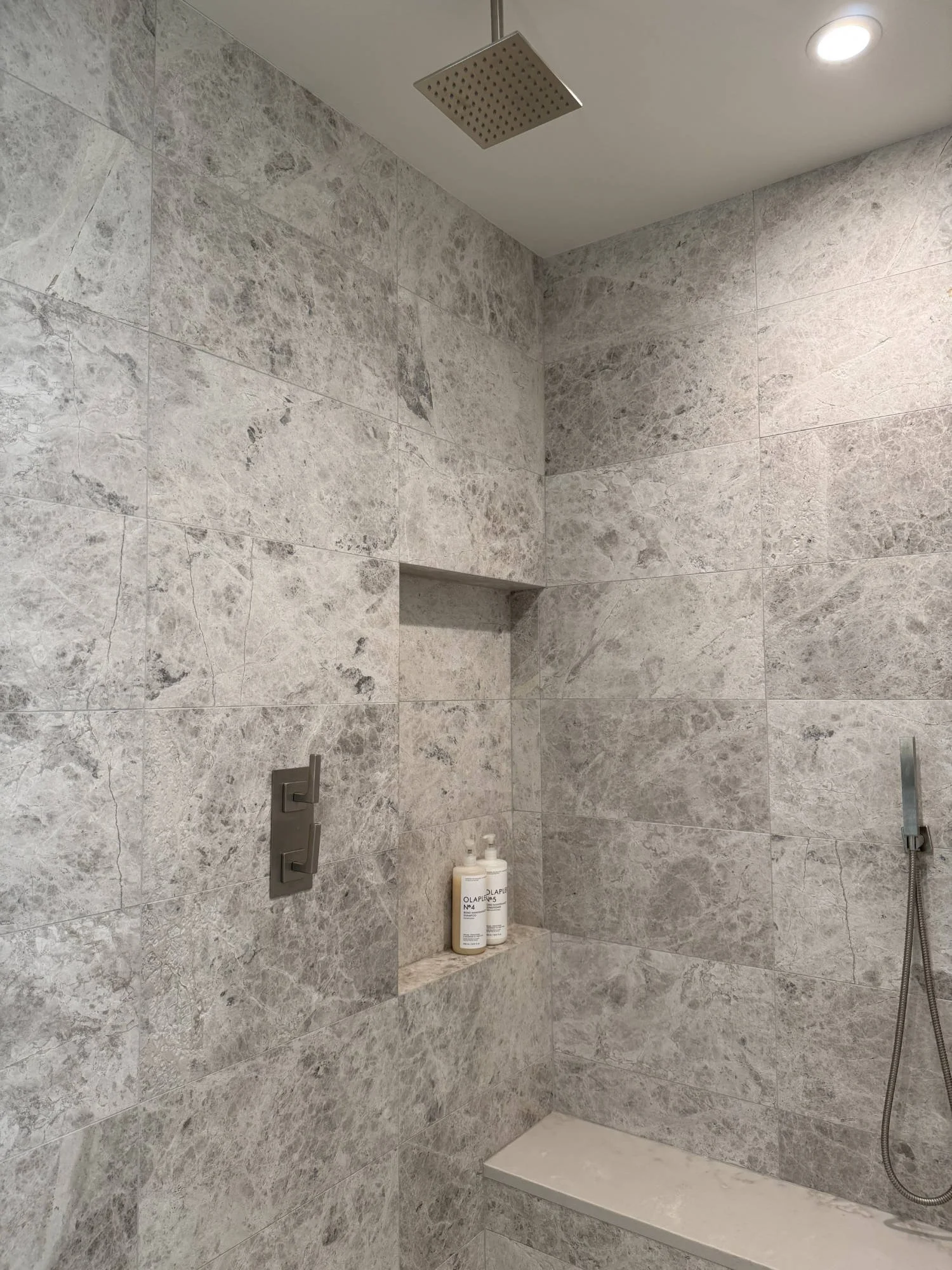 Walk-in shower clad in large-format grey stone with a recessed niche and rain shower