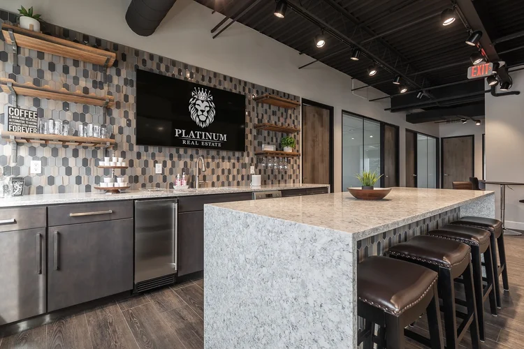 Coffee bar with a quartz waterfall island, bar stools, open shelving on a patterned tile wall and the Platinum Real Estate logo