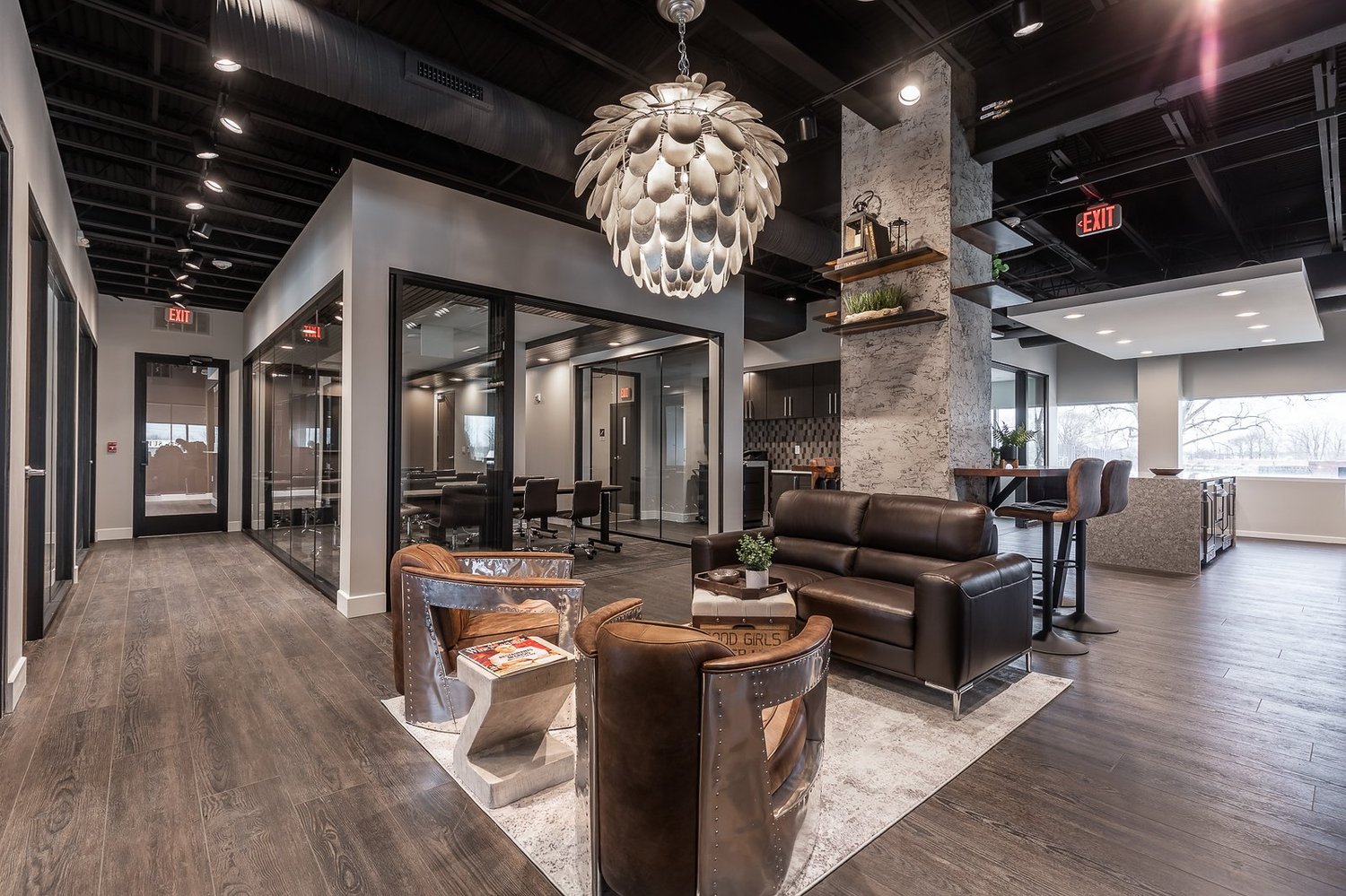 Central lounge under a large sculptural pendant light, with leather seating and glass-walled offices around it