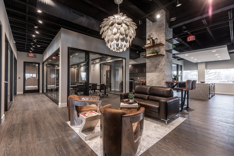 Central lounge under a large sculptural pendant light, with leather seating and glass-walled offices around it