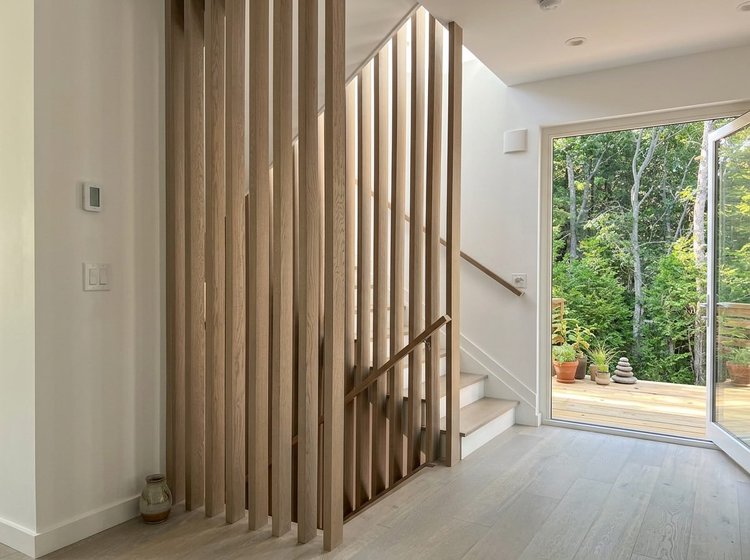 Stair screened by tall vertical oak slats, beside glass doors that open to a wooded deck