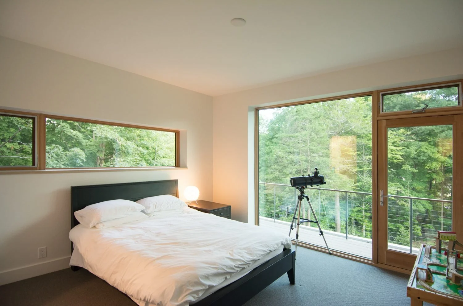 Guest bedroom in New Canaan, Connecticut, with a clerestory window and a glass door to a balcony above the trees