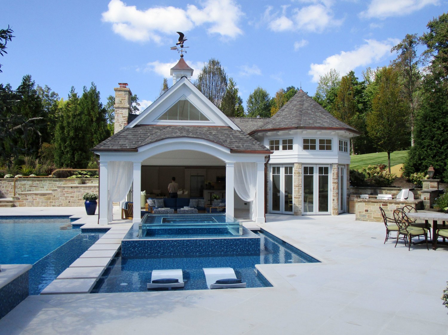 Pool house with arched loggia and white curtains, seen across the pool and spa