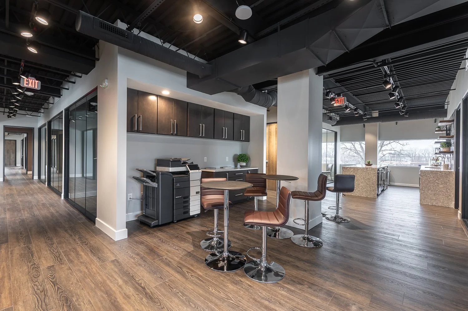 Work café with high-top tables and stools near a copy station and dark wood cabinetry under an open ceiling