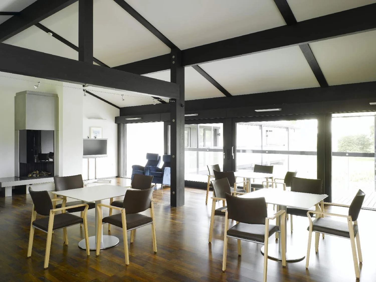 Common dining room with wood floors, exposed beams, tables and chairs, and views to the garden
