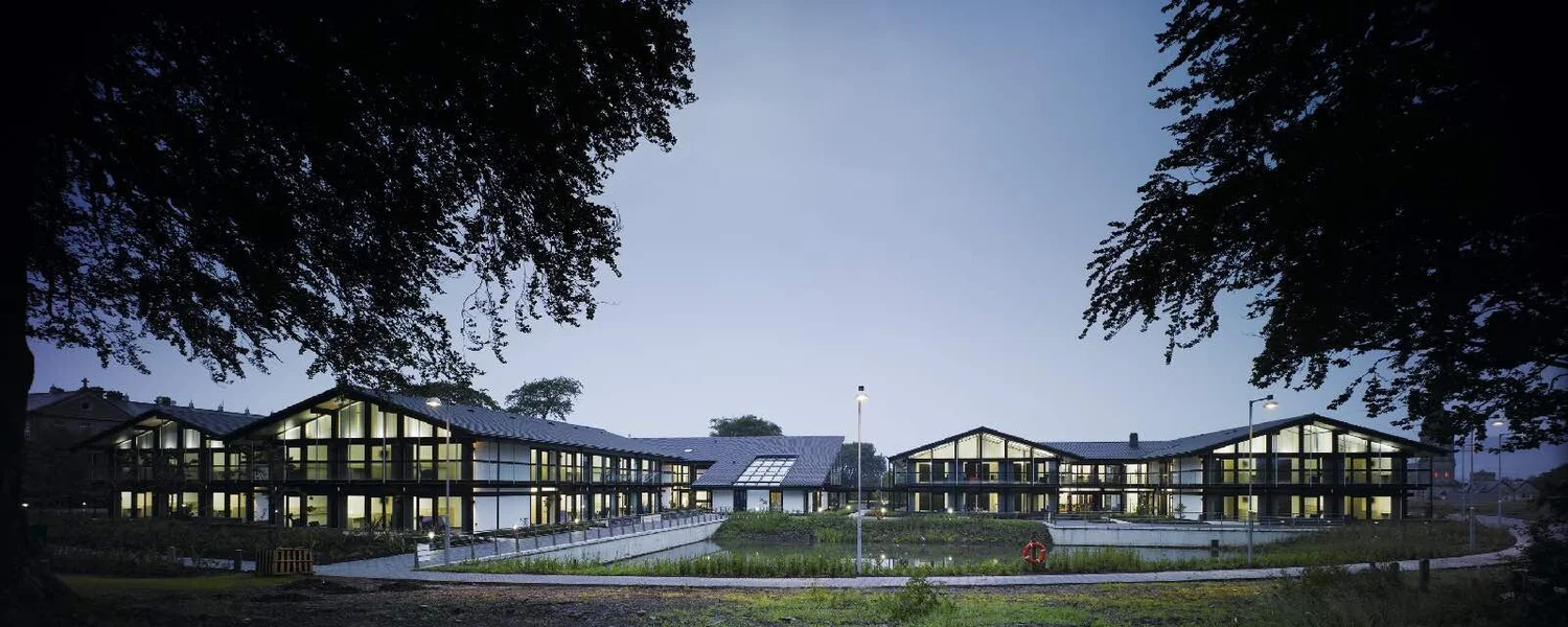 Nazareth House at dusk: the central building and two residential wings under shallow gabled roofs, framed by trees