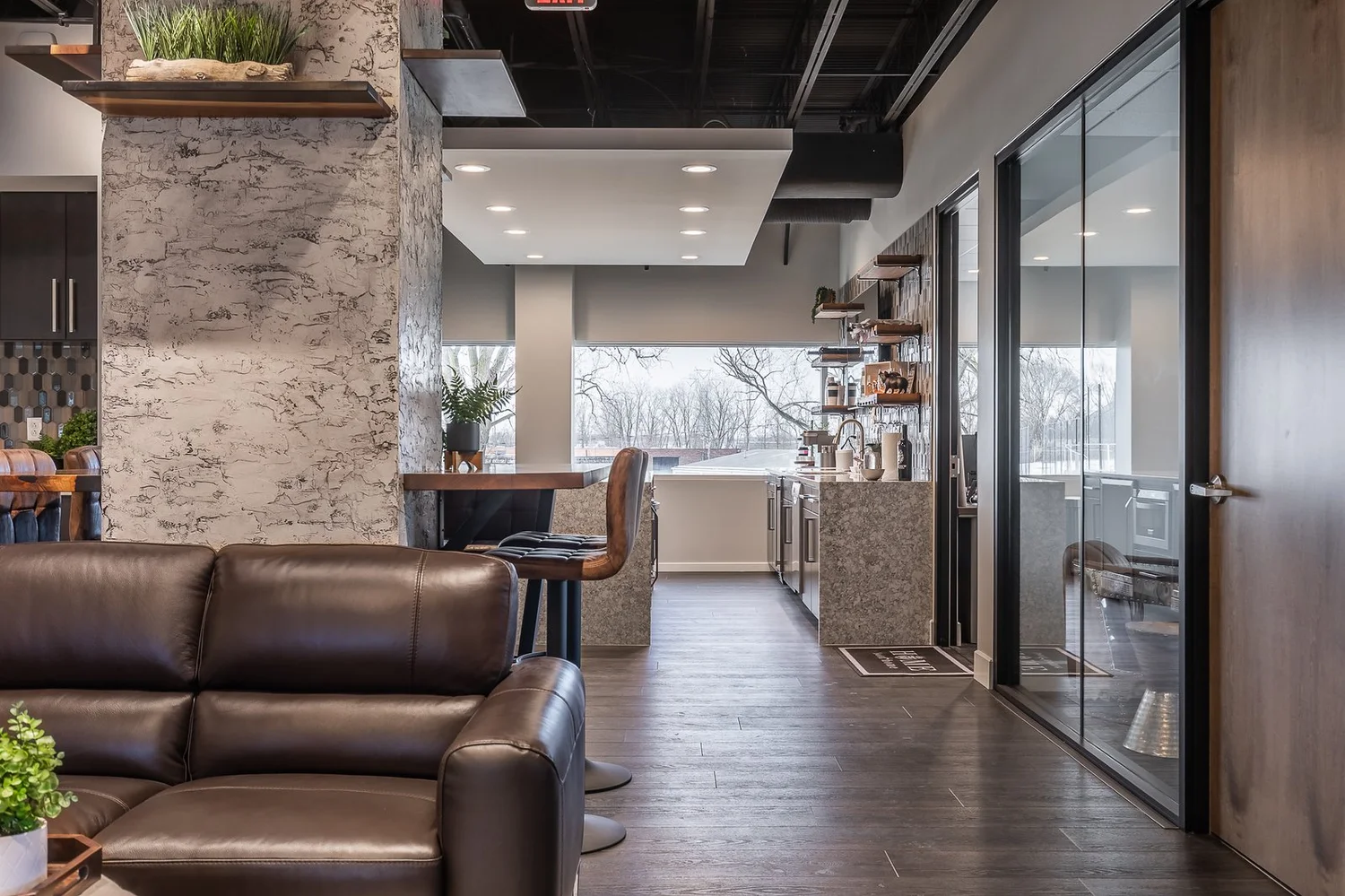 Leather sofa in front of a stone-clad column, with high-top seating and glass offices along the windows