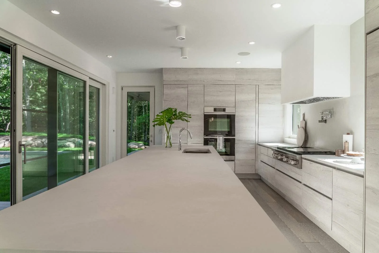 Modern kitchen with light wood cabinets, a long white island and glass doors to the garden