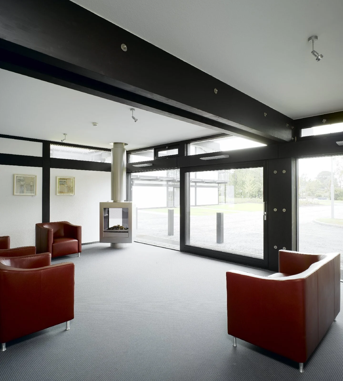 Group living room with red armchairs, a freestanding fireplace and floor-to-ceiling windows