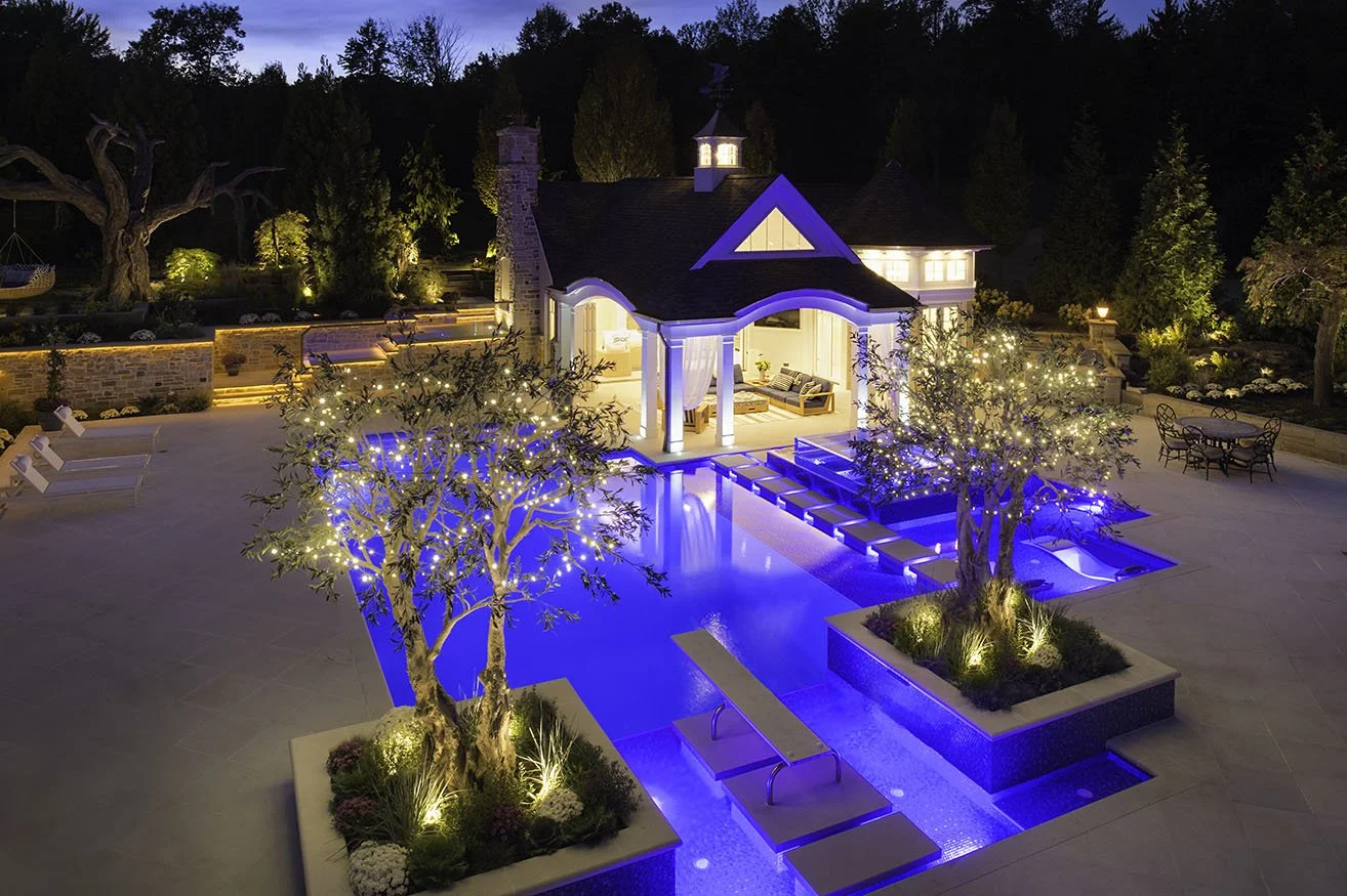 Pool house at night with lit pool, raised planters and trees in the terrace