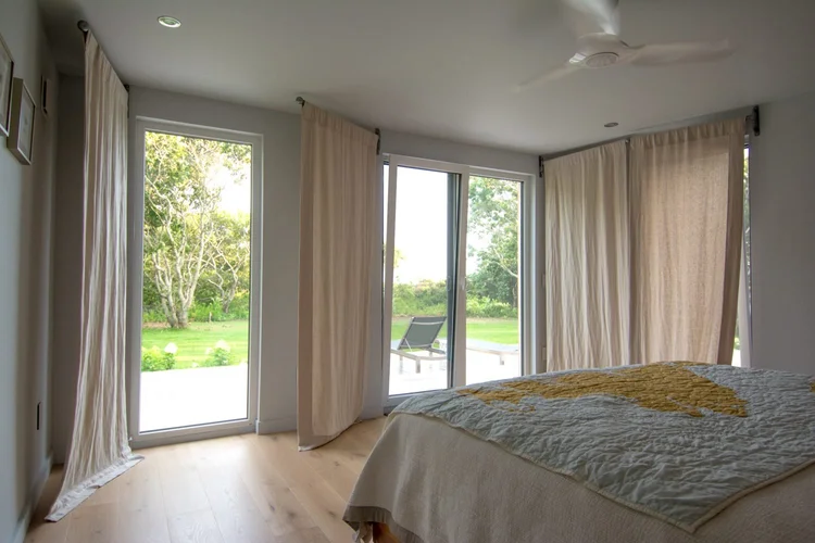 Bedroom on Martha’s Vineyard with linen curtains and glass doors that open to the lawn and terrace